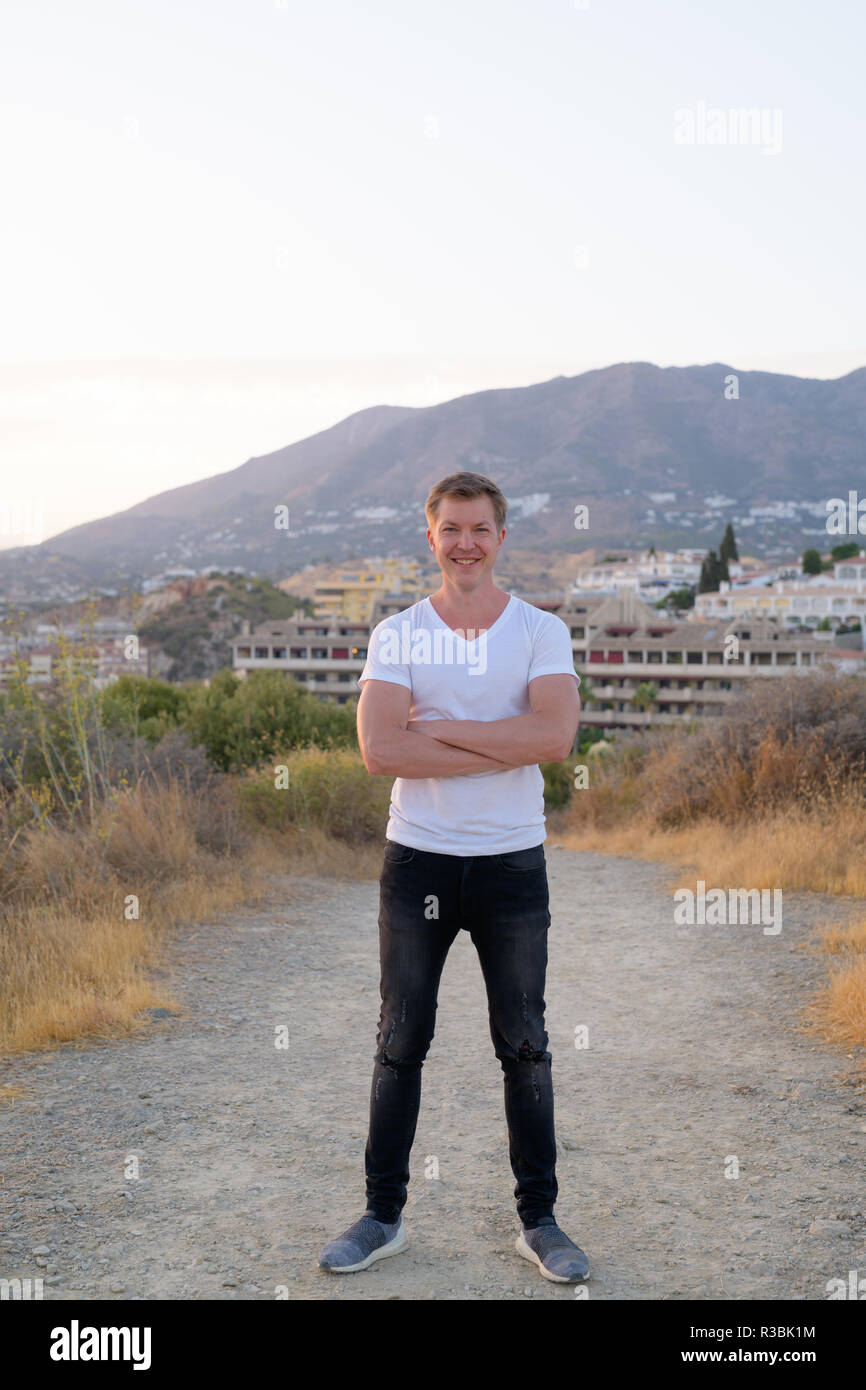 Junge Attraktive touristische Mann lächelnd beim Stehen auf der Spitze des Hügels Stockfoto