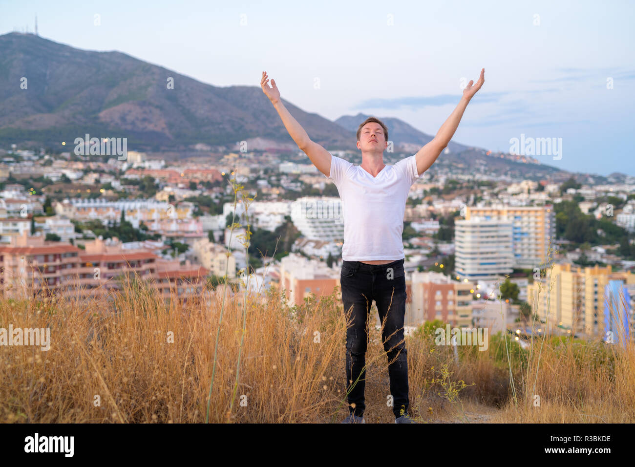 Junge touristische Mann mit geschlossenen Augen und offenen Armen beim Stehen auf der Spitze des Hügels Stockfoto