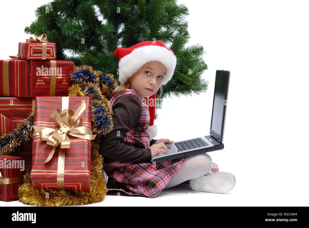 Kleines Mädchen in Santa Claus Cap mit einem Laptop und Weihnachten Geschenke auf weißem Hintergrund, isoliert Stockfoto