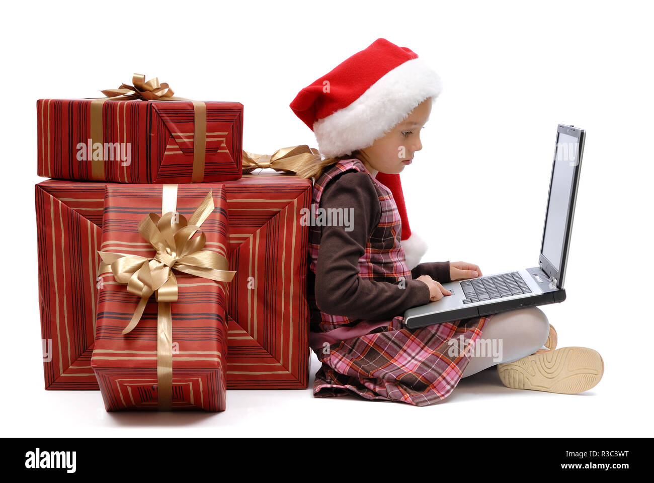 Kleines Mädchen in Santa Claus Cap mit einem Laptop und Weihnachtsgeschenk auf weißem Hintergrund, isoliert Stockfoto