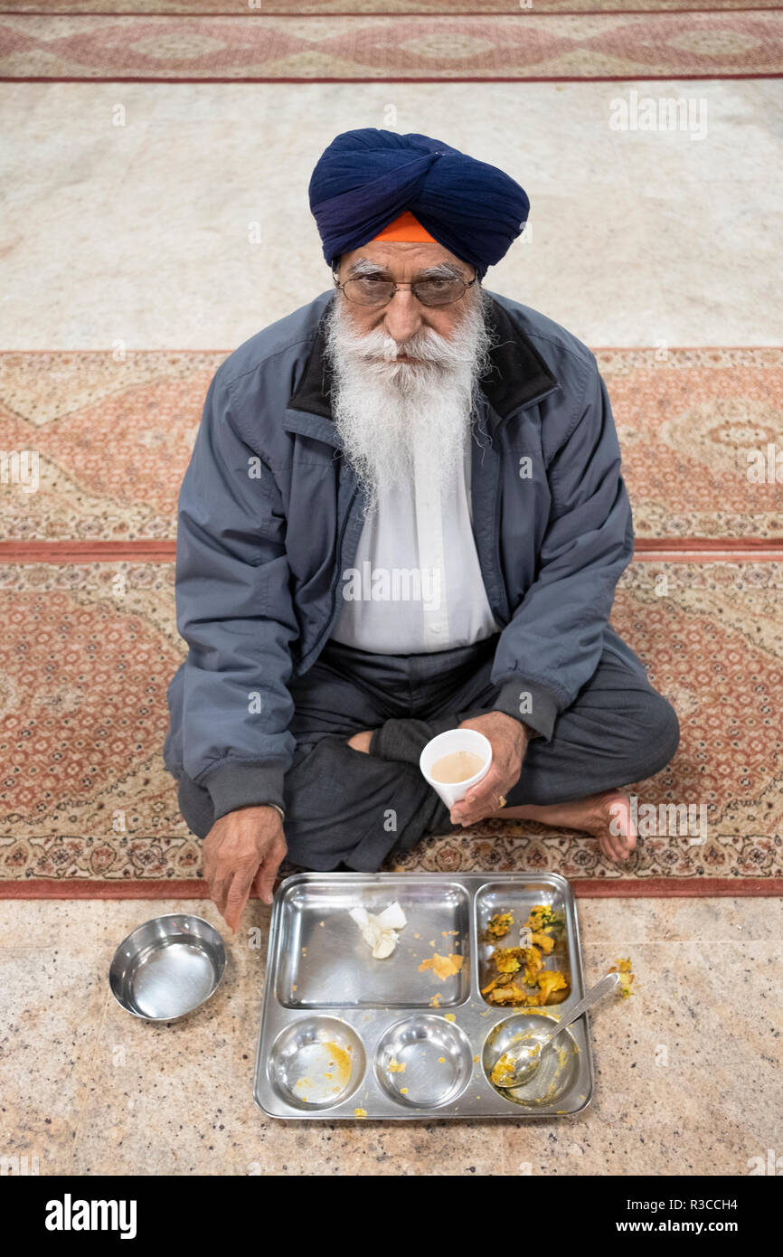 Eine ältere Sikh Mann mit einem weißen Bart und Turban essen eine kostenlose Mahlzeit in einem langar in einem Sikh-tempel in Queens, New York. Stockfoto