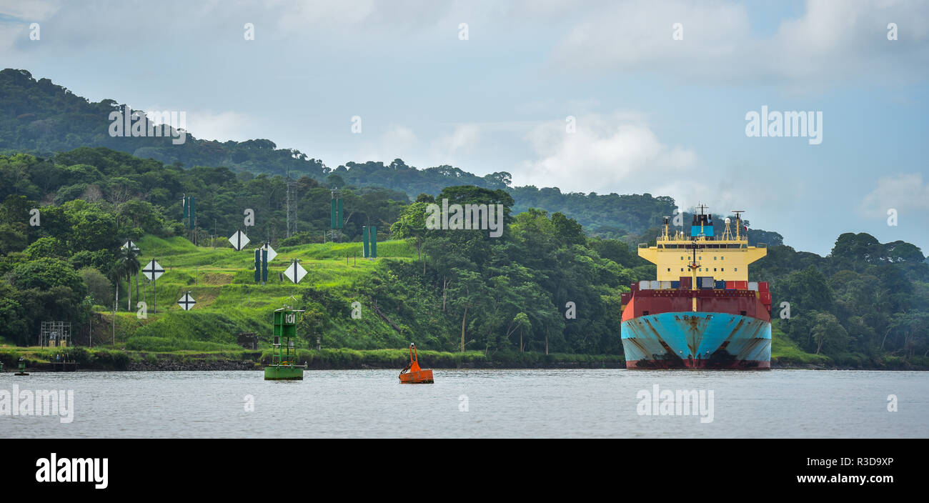 Ein großes Frachtschiff macht seinen Weg durch den Panamakanal, gesäumt von grünen Dschungel auf beiden Seiten. Stockfoto