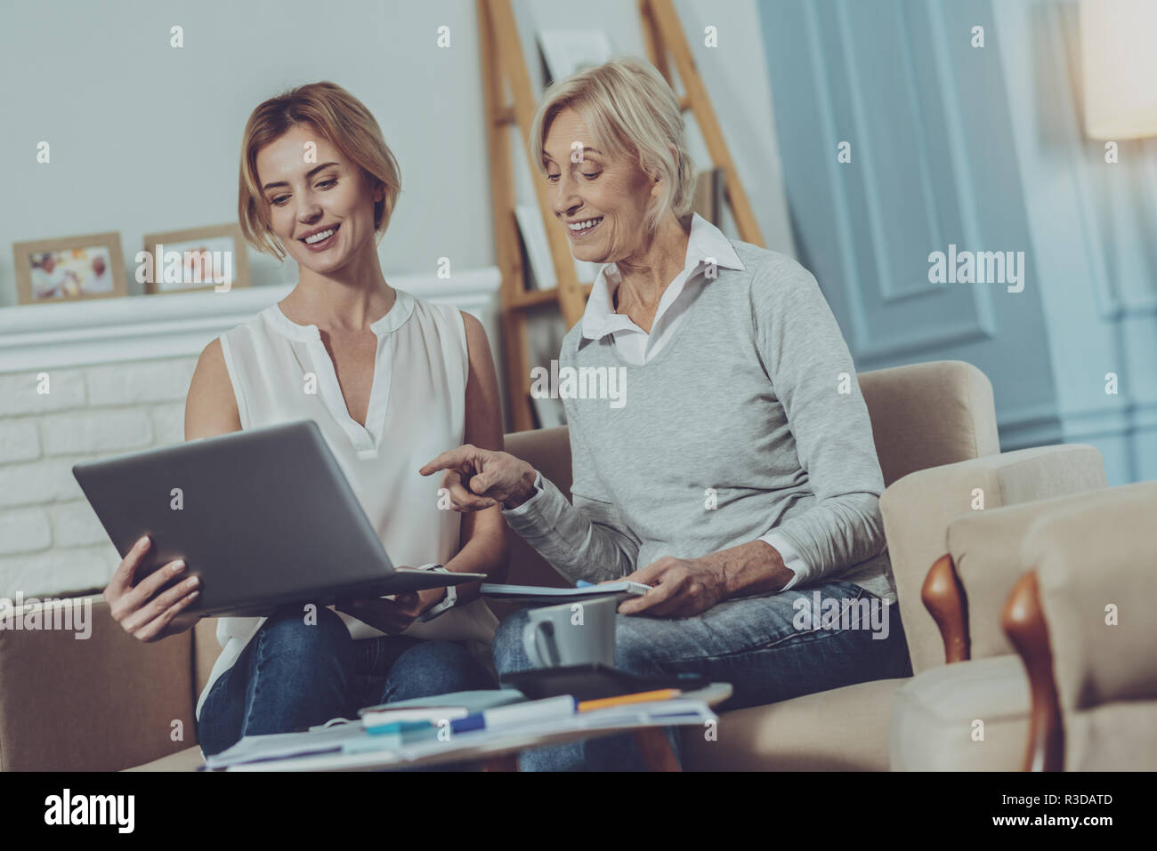 Angenehme Dialog. Liebenswerte ältere Dame mit Notizblock in die Hände am Laptop Bildschirm junger erfreut, Frau neben ihr sitzt, beim Besprechen Stockfoto