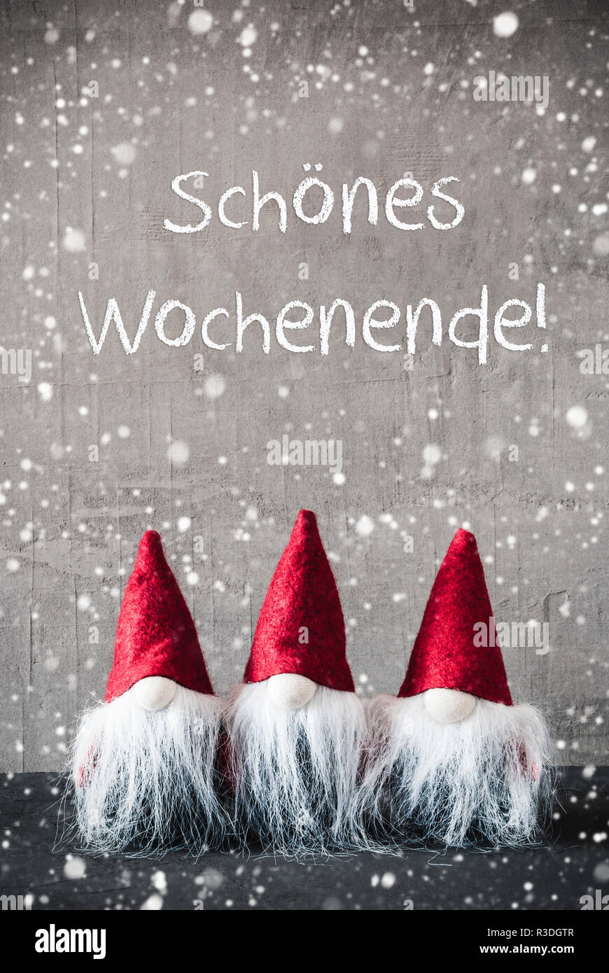 Drei graue Zwerge mit deutschen Text schoenes Wochenende bedeutet Happy Weekend und roter Zipfelmütze. Urban Zement Hintergrund mit Schneeflocken. Vertikale Fo Stockfoto