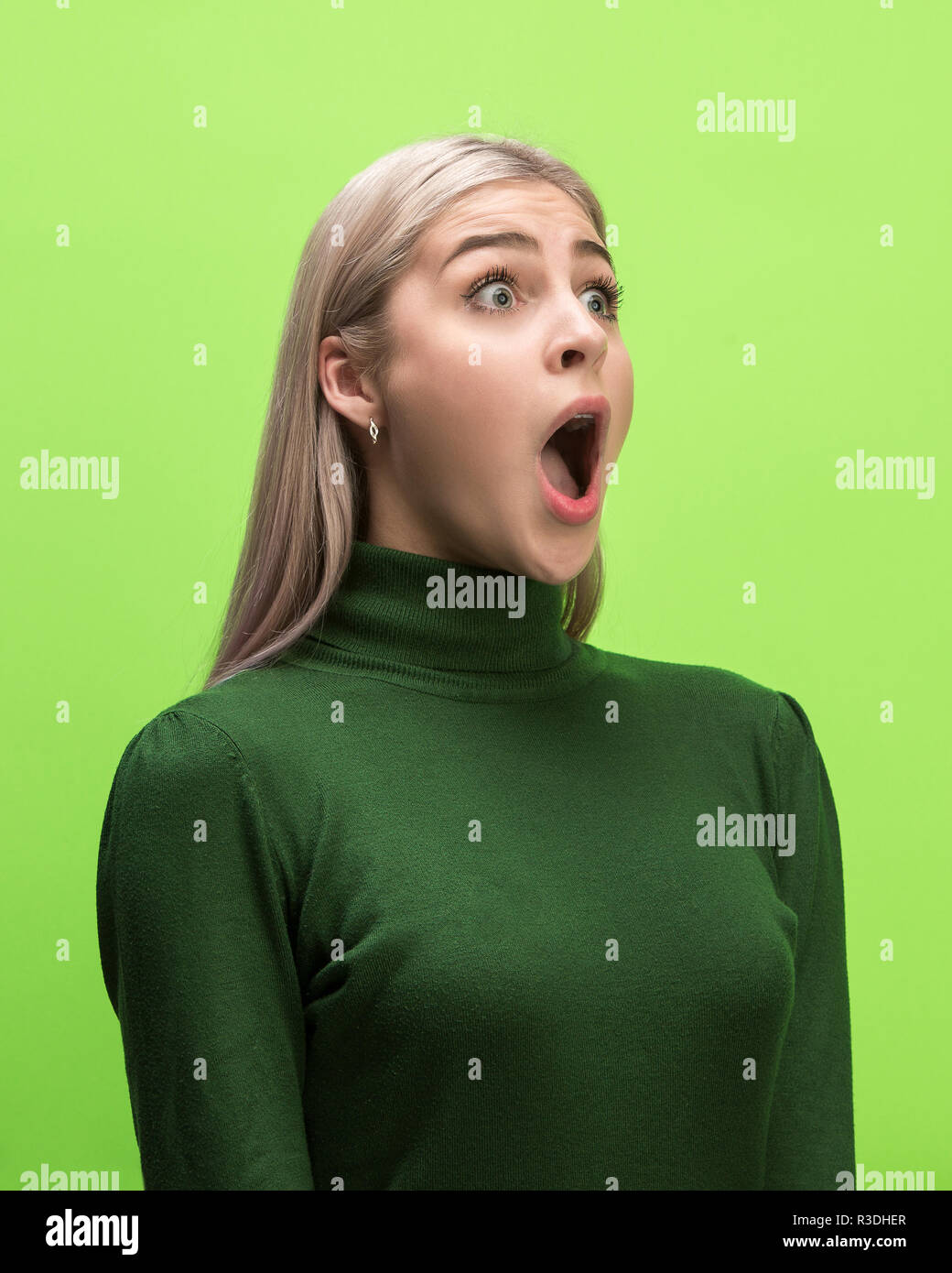 Das überrascht und erstaunt junge Frau schreiend mit offenen Mund auf grünem Hintergrund isoliert. Konzept der Schock angesichts der menschlichen Emotion Stockfoto
