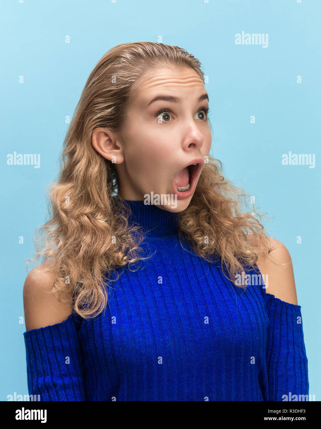 Das überrascht und erstaunt junge Frau schreiend mit offenen Mund auf blauem Hintergrund isoliert. Konzept der Schock angesichts der menschlichen Emotion Stockfoto