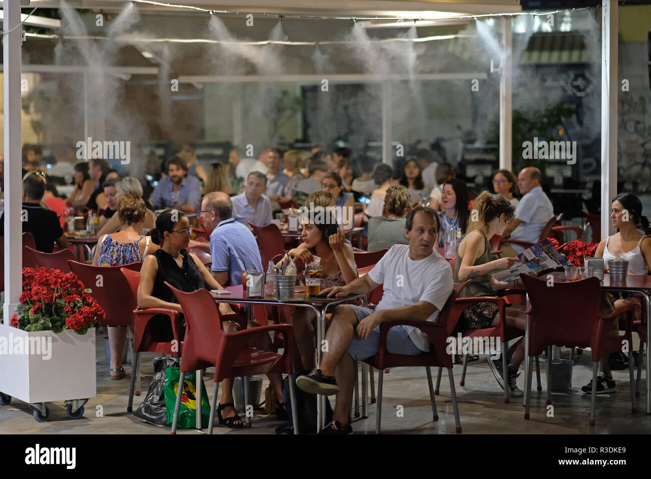 Menschen sitzen in einer spanischen Bar, Restaurant mit Nebel gesprüht wird, um sie zu kühlen. Sevilla. Stockfoto