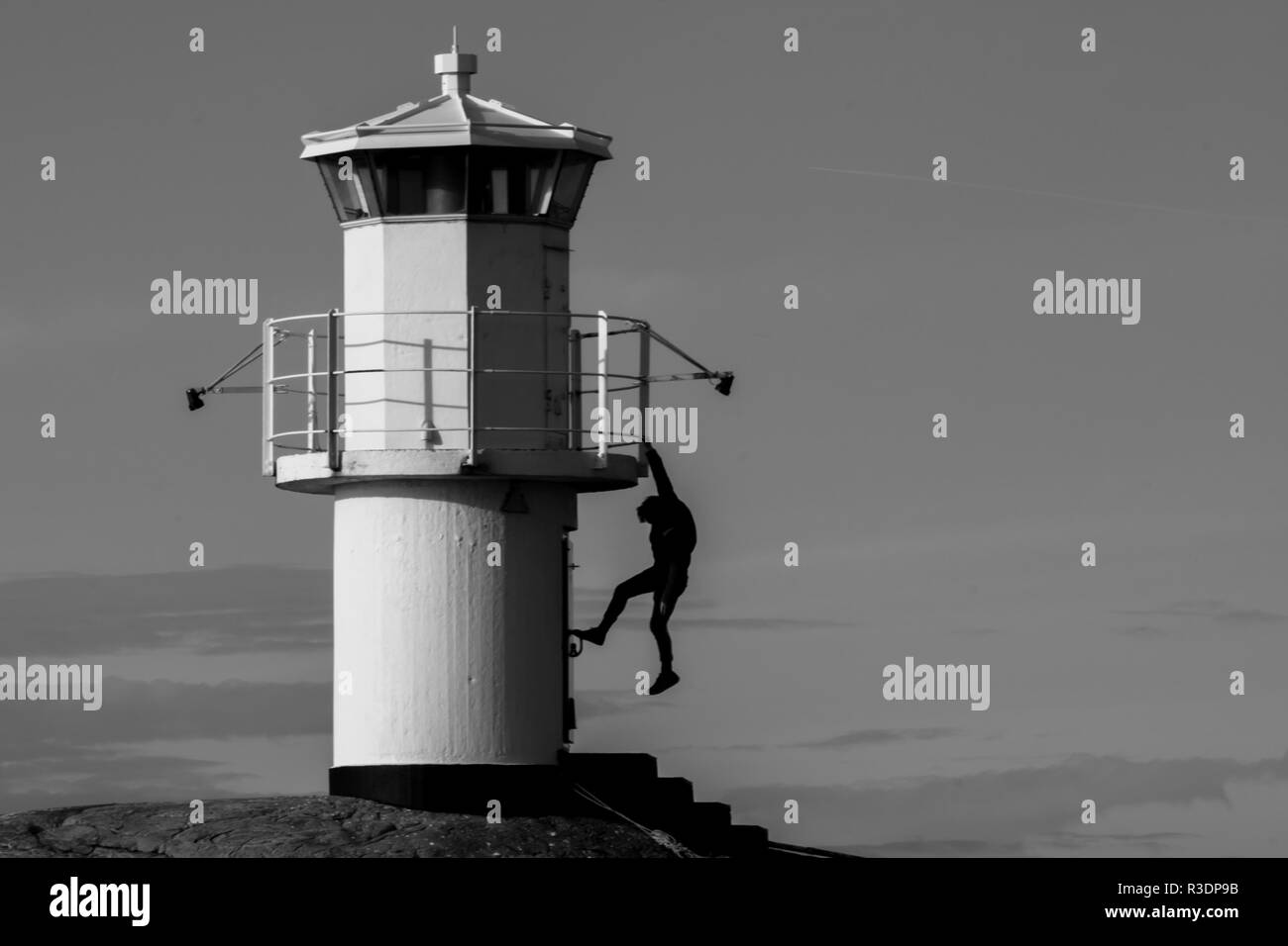 Die Silhouette eines jungen Menschen hängen von einem Leuchtturm mit einer Hand in Schwarz in Weiß Stockfoto