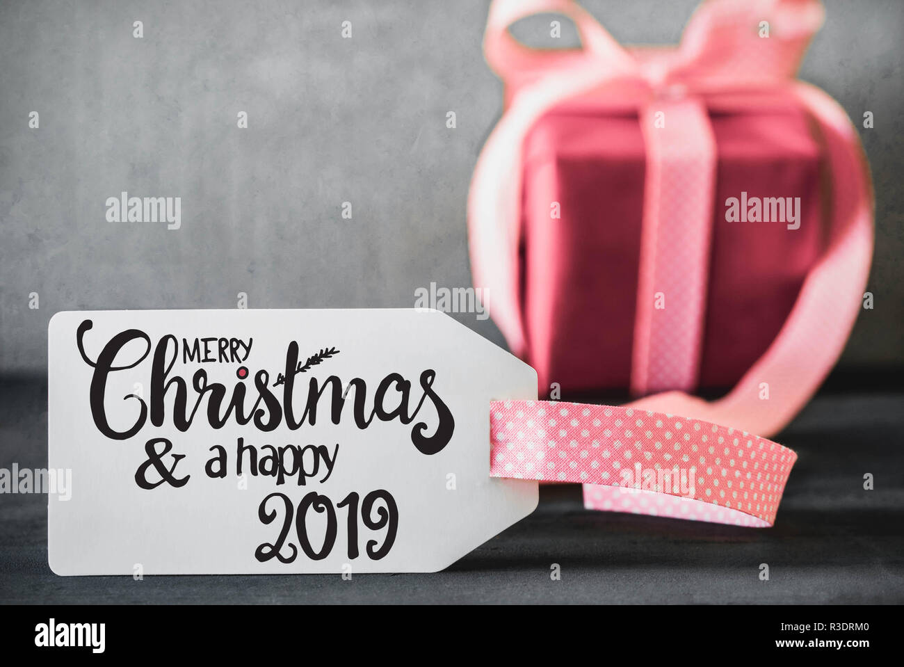 Etikett mit englischen Kalligraphie frohe Weihnachten und einen guten Rutsch ins Jahr 2019. Ein rosa Geschenk mit Ribbn. Zement Hintergrund. Stockfoto
