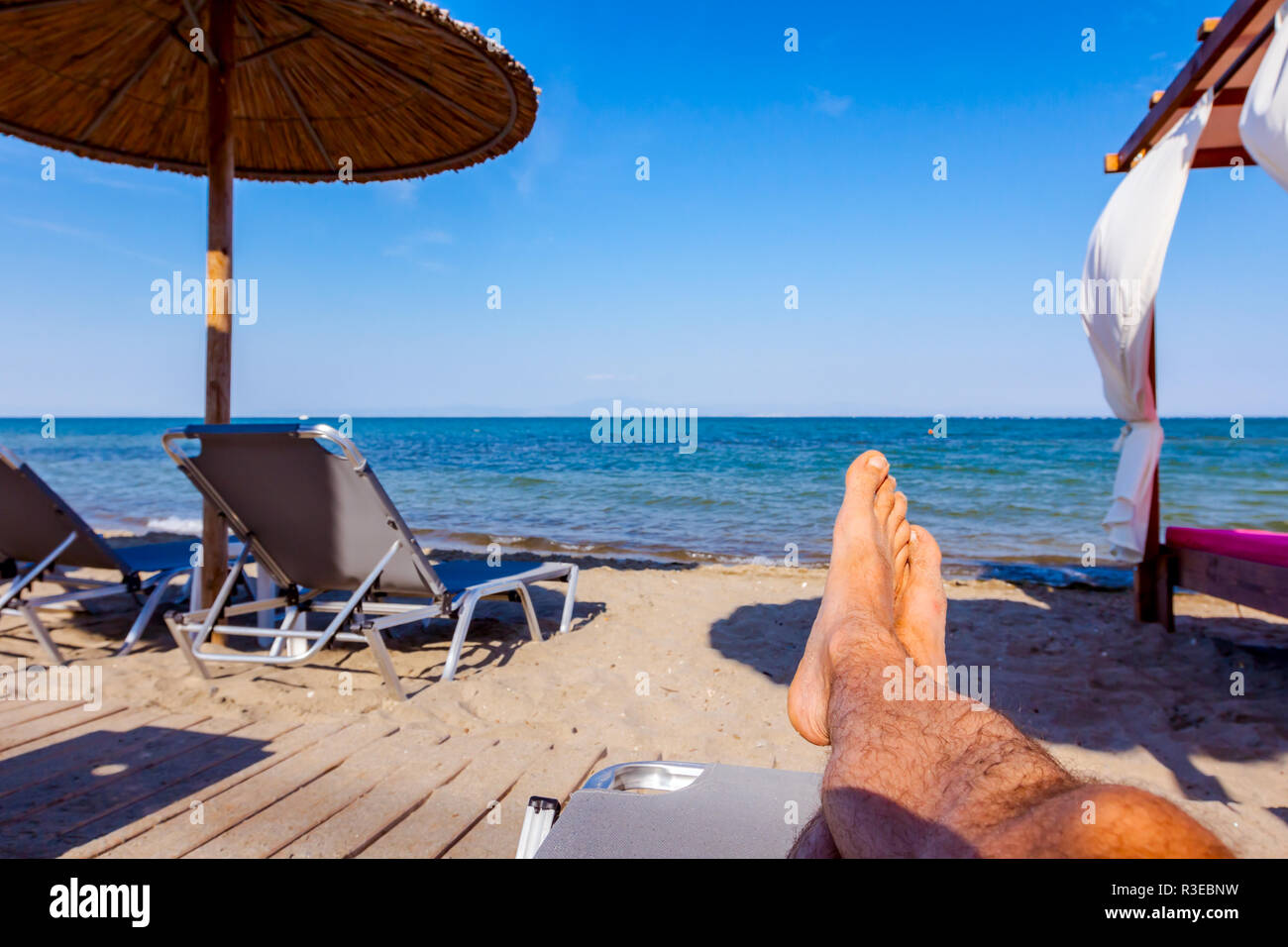 Man Beine bis zum Sonnenbaden ist liegend sorglos in Liege neben der Küste, am öffentlichen Strand. Stockfoto