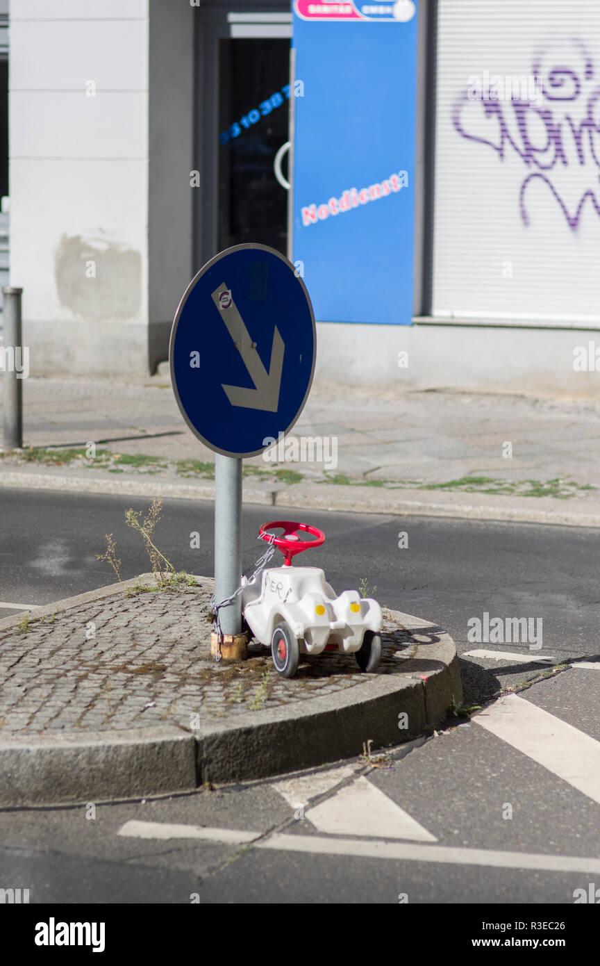 Die kleinen weißen Kunststoff Automobil angekettet an ein Wegweiser auf der Straße in Berlin, Deutschland mit Graffiti an den Wänden im Hintergrund Stockfoto