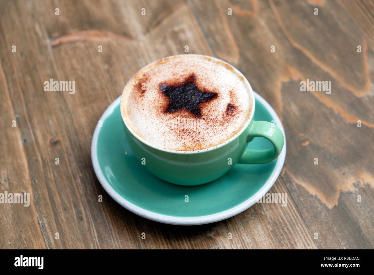 Tasse Cappuccino mit einem Christmas Star Design von Schokolade bestreut mit aufgeschäumter Milch in grün Tasse & Untertasse auf holztisch UK KATHY DEWITT Stockfoto