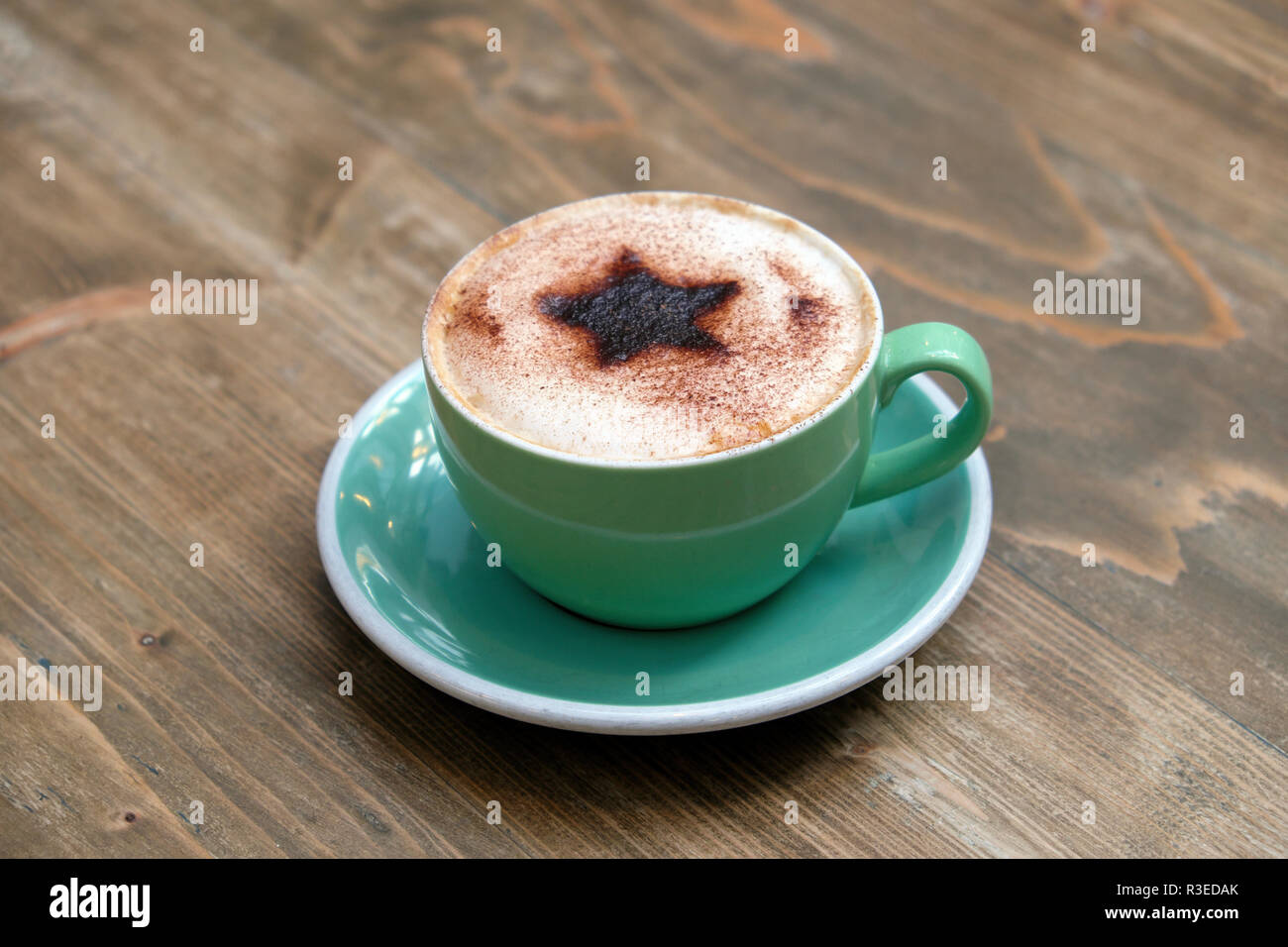 Festliche Tasse Cappuccino mit einem Christmas Star Design von Schokolade bestreut mit aufgeschäumter Milch in eine grüne Tasse und Untertasse im Shop UK KATHY DEWITT Stockfoto