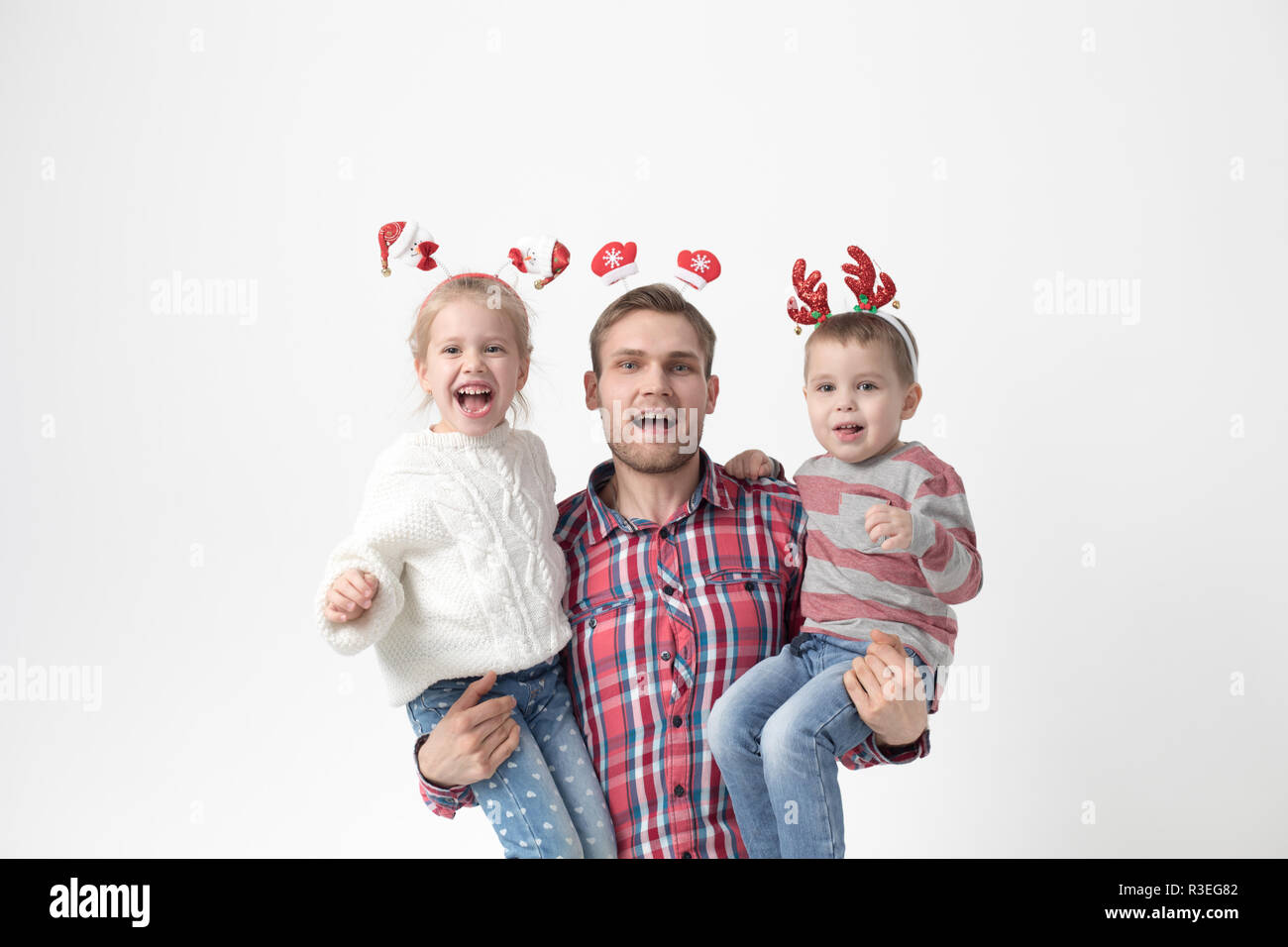Vater hält die Kinder in seine Arme auf einem weißen Hintergrund. Happy Family im lustig Weihnachten Stirnbänder. Stockfoto