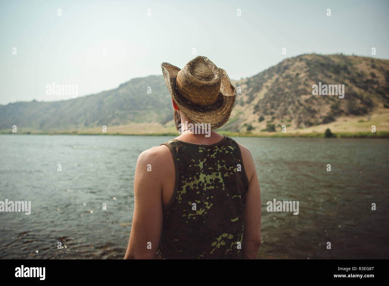 Ehrliches Foto eines Mannes mit Cowboyhut, der einen Blick auf den Fluss hat und die Aussicht genießt. Fläche in nicht sichtbar. Stockfoto