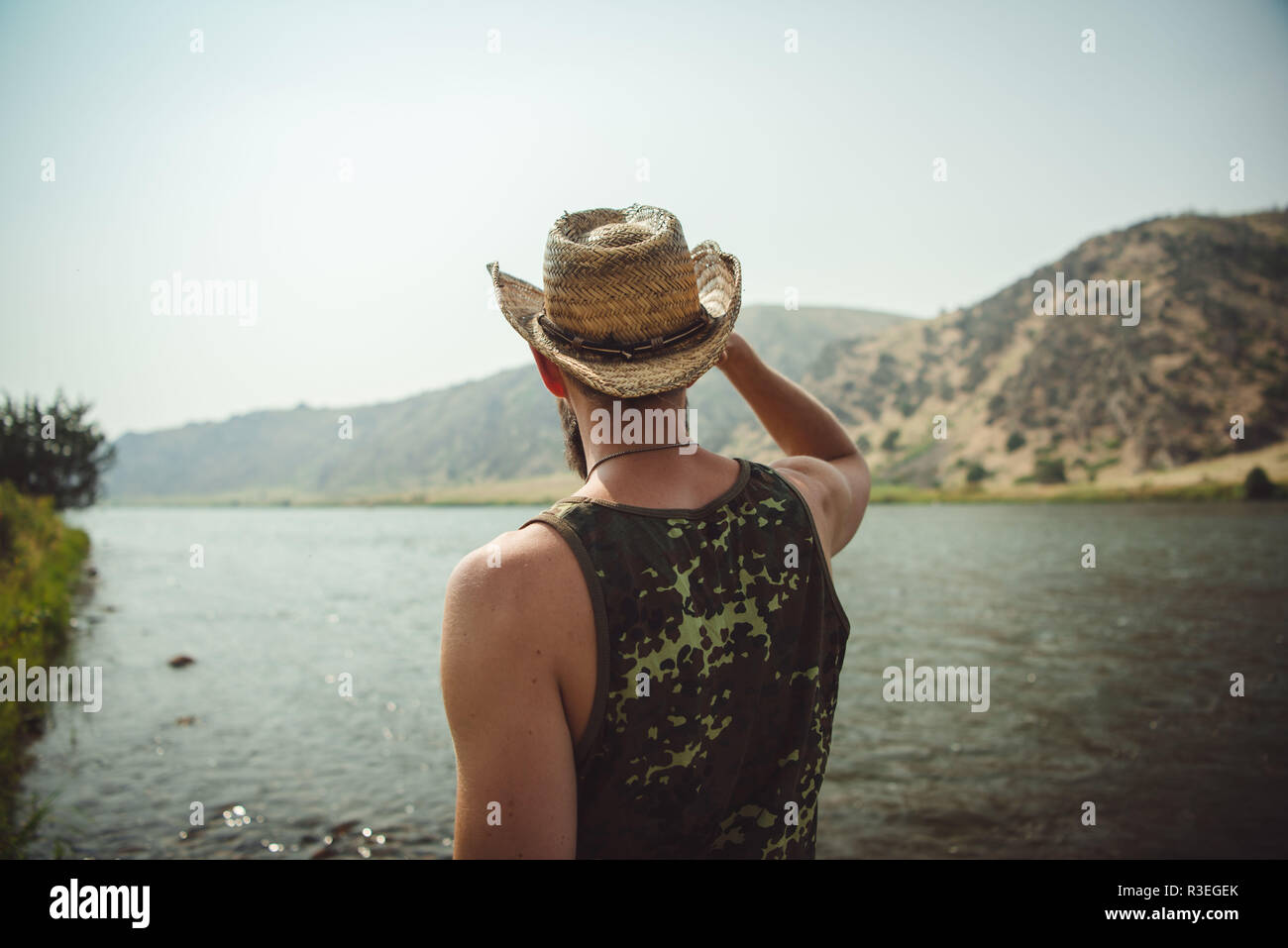 Ehrliches Foto eines Mannes mit Cowboyhut, der einen Blick auf den Fluss hat und die Aussicht genießt. Fläche in nicht sichtbar. Stockfoto