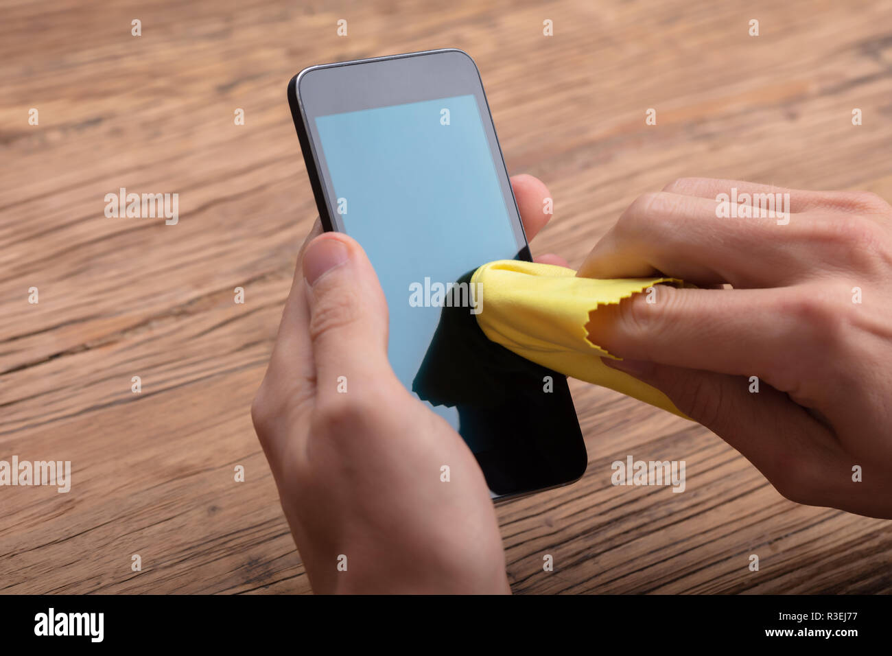 Mann Reinigung Mobiltelefon mit gelben Tuch über Holz- Schreibtisch Stockfoto