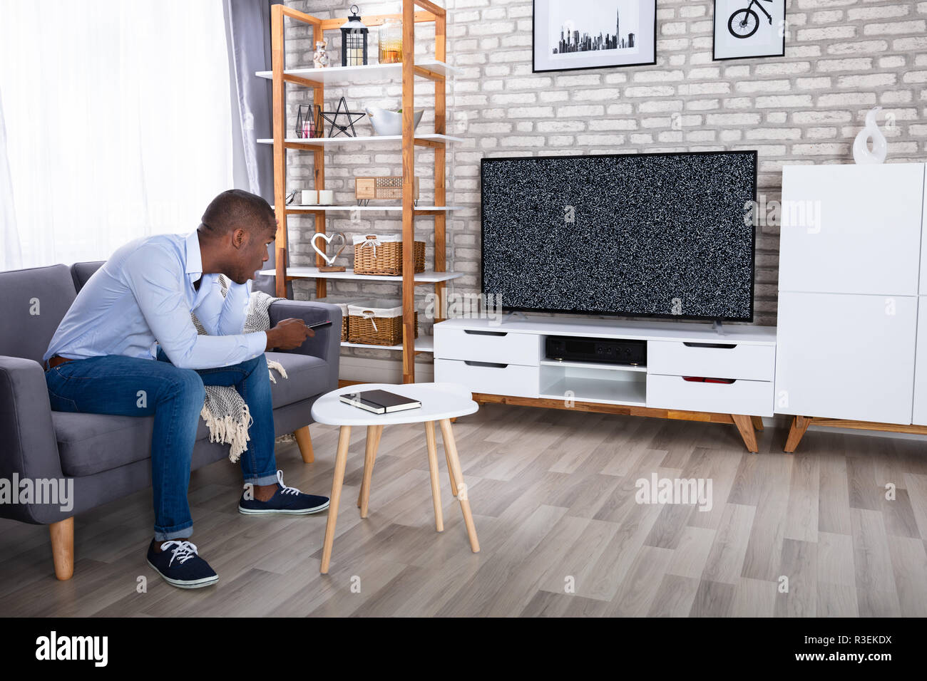 Afrikanische Mann sitzt auf dem Bett, Fernseher mit Kein Signal Stockfoto
