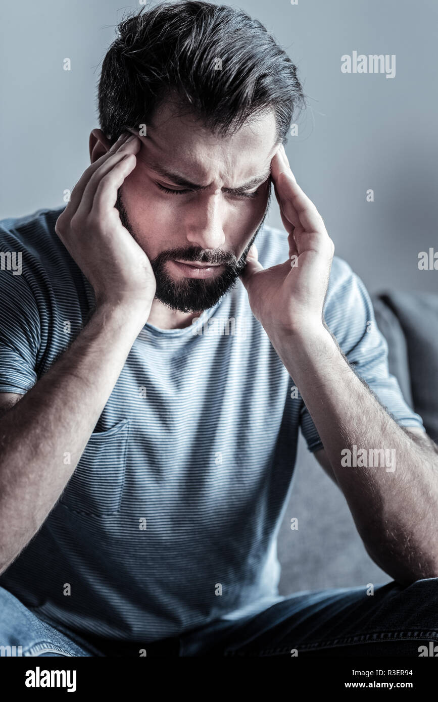 Haben Kopfschmerzen. Ernsthafte bärtigen Mann halten die Augen geschlossen und seine Schläfen massieren beim Denken über sein Problem Stockfoto