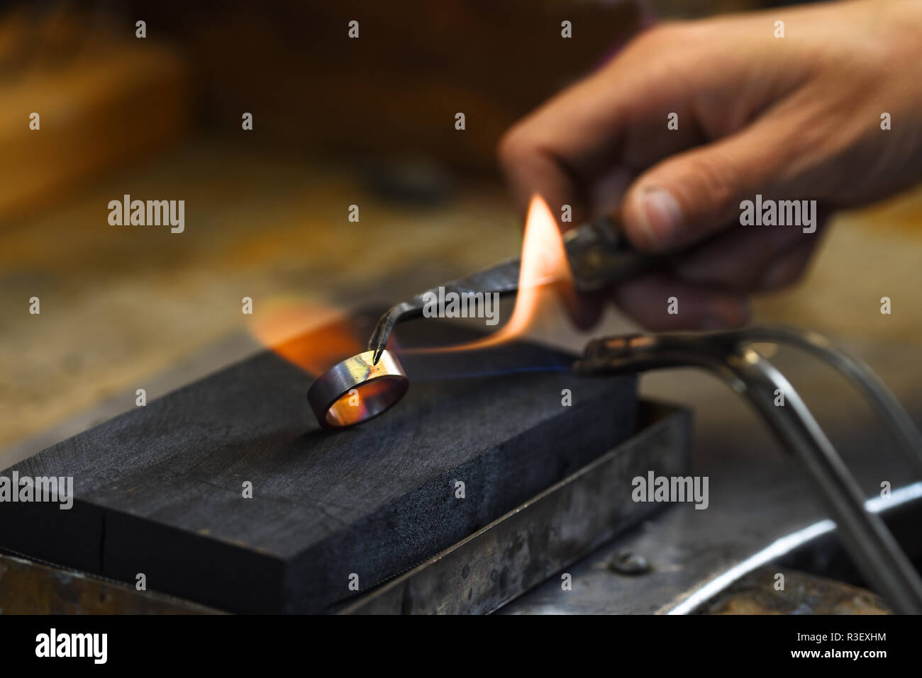 Goldschmied Hand leuchtet eine goldene Hochzeit Ring mit einer Gasflamme, kopieren Platz im dunklen Hintergrund, ausgewählte konzentrieren, enge Tiefenschärfe Stockfoto