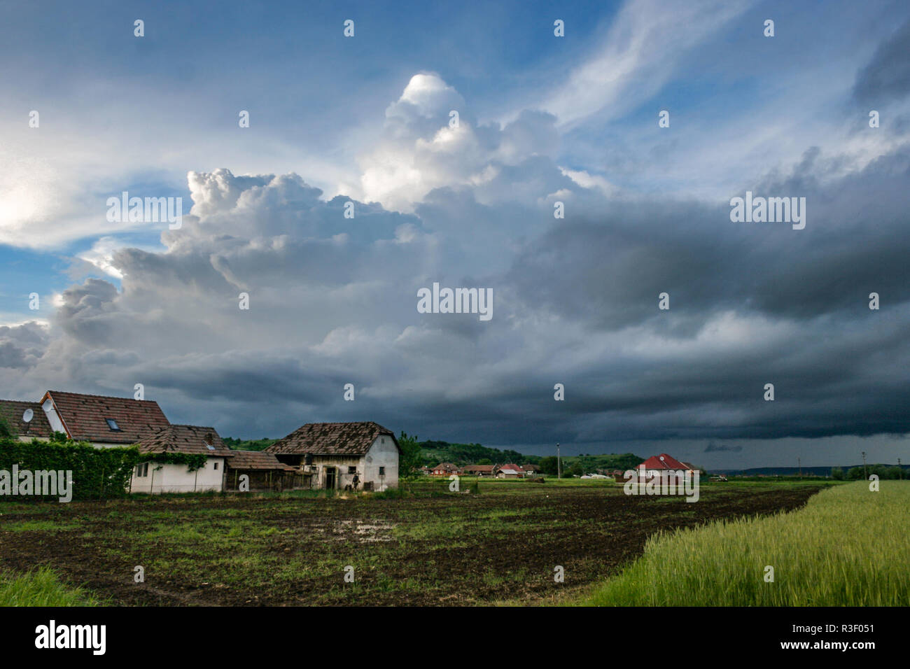 Sturmwolken sammeln sich über ländlichen Bauernhäusern und grünen Feldern im Mures-Tal, Transsilvanien, Rumänien. Malerischer Landschaftsstil Stockfoto