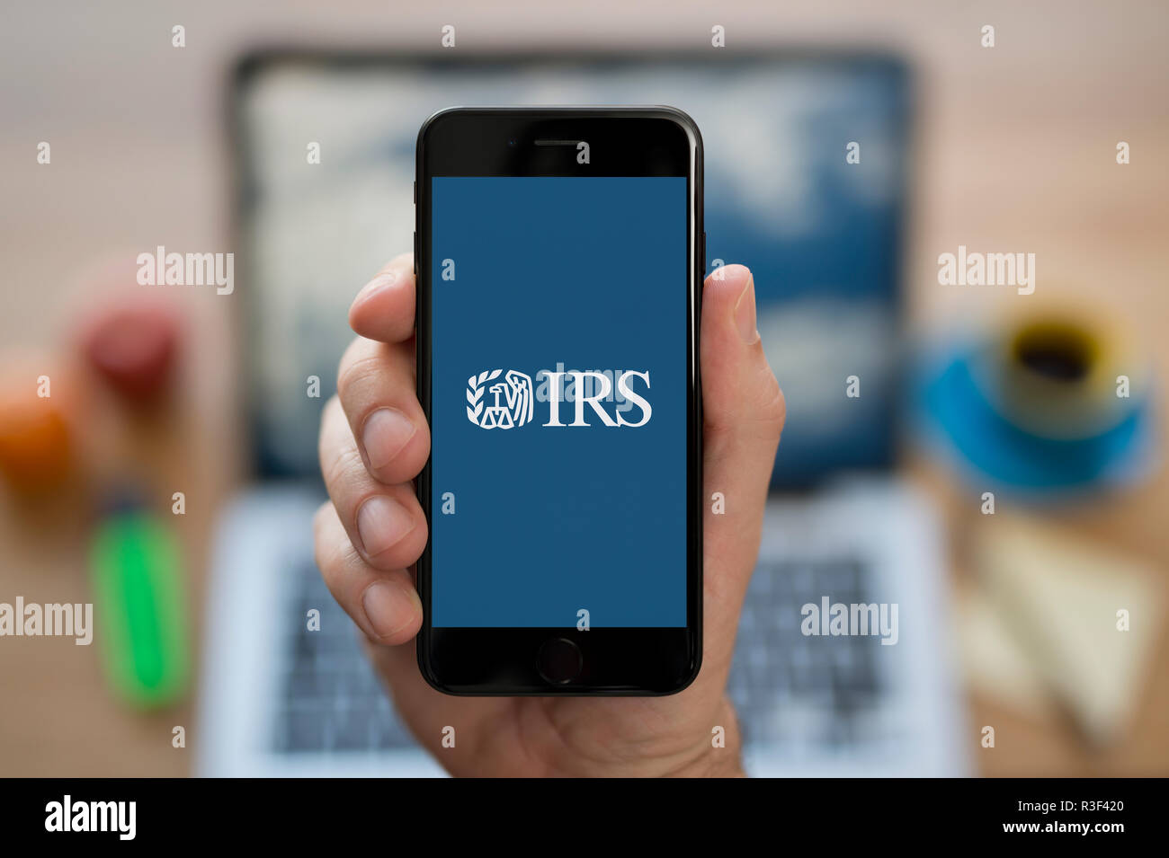 Ein Mann schaut auf seinem iPhone die Anzeige der Internal Revenue Service (IRS) Logo, während saß an seinem Computer Schreibtisch (nur redaktionelle Nutzung). Stockfoto