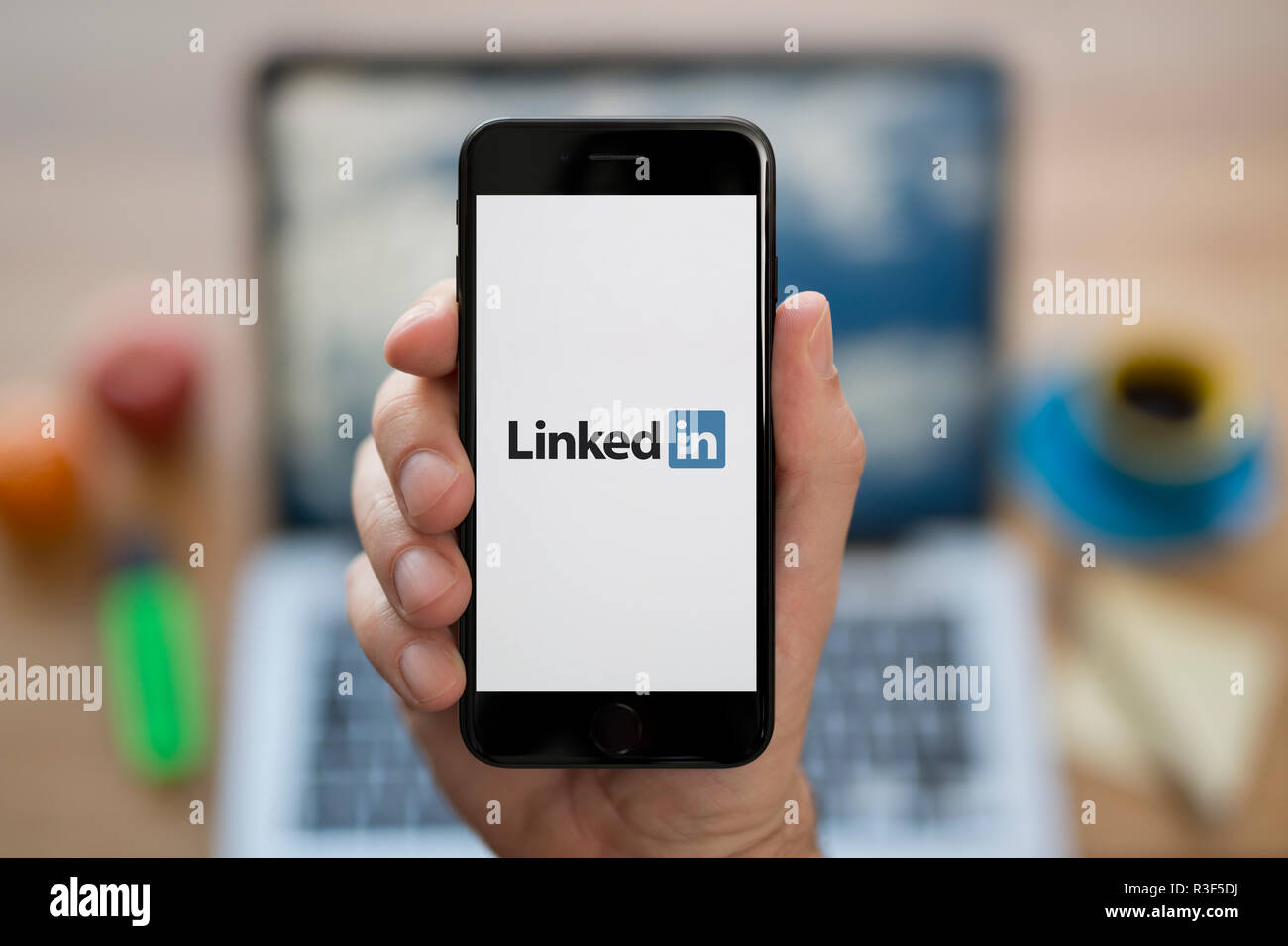 Ein Mann schaut auf seinem iPhone die zeigt die LinkedIn logo, während saß an seinem Computer Schreibtisch (nur redaktionelle Nutzung). Stockfoto