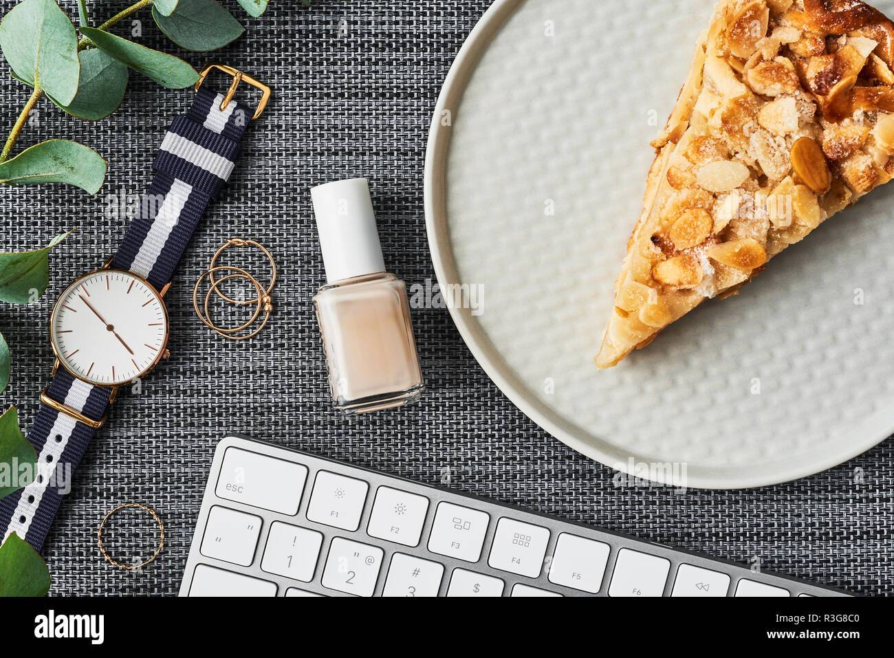 Gemütliche business Zusammensetzung mit weißen Computer Tastatur, Nagellack, Ringe, Eukalyptus, Women's Watch und Apfelkuchen auf die Platte über der Grauen backgroun Stockfoto
