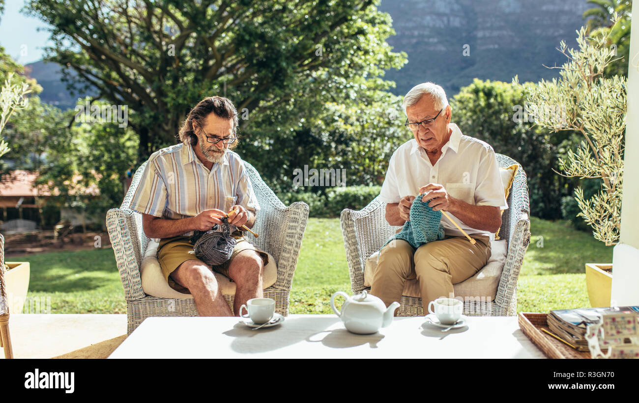 Zwei alte Männer sitzen im Innenhof und Stricken. Ältere Freunde sitzen auf Stühlen und Kitting Kammgarn tragen. Stockfoto