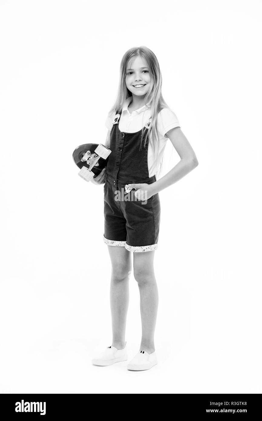 Kleines Mädchen lächeln mit Skate Board auf Weiß isoliert. Kind skater lächelnd mit Longboard. Skateboard kid in rosa Overall. Sportliche Aktivität und Energie. Stockfoto