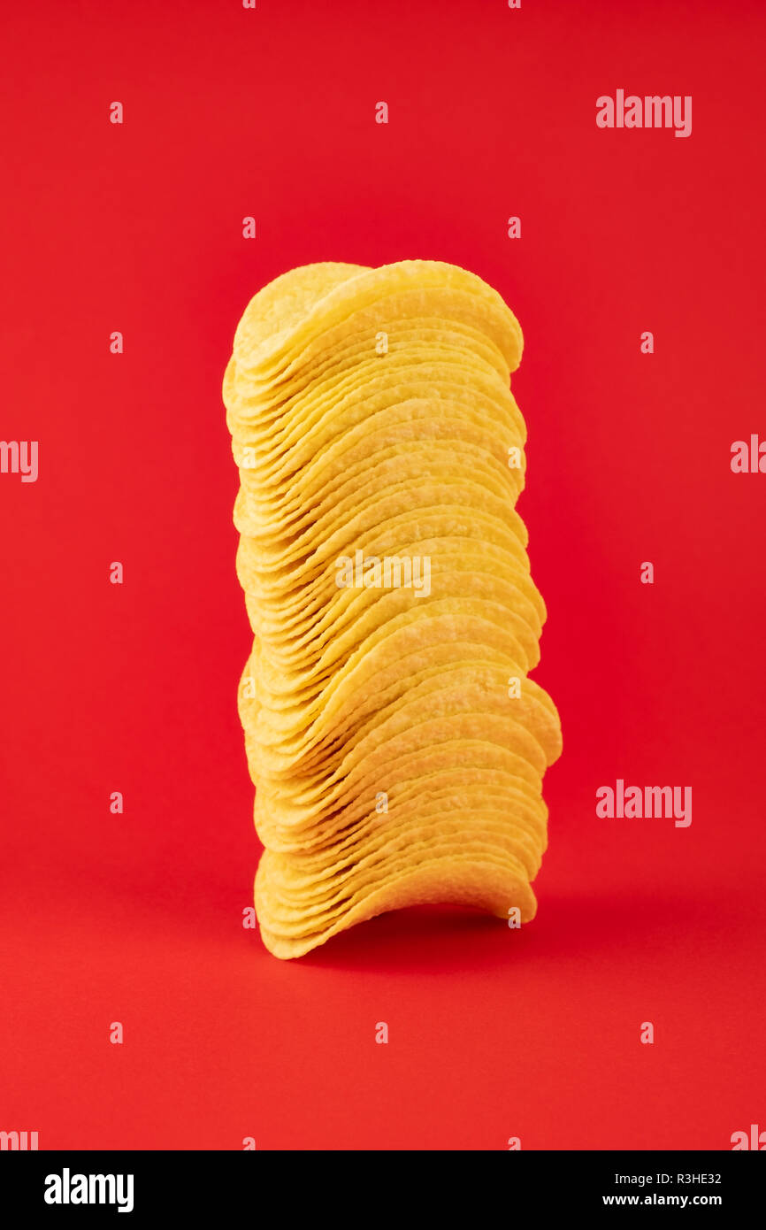 Stapel von Kartoffelchips in hellen roten Hintergrund. Minimalistischer Bild von Aufmerksamkeitsstarke fast food in lebendigen Farben Stockfoto