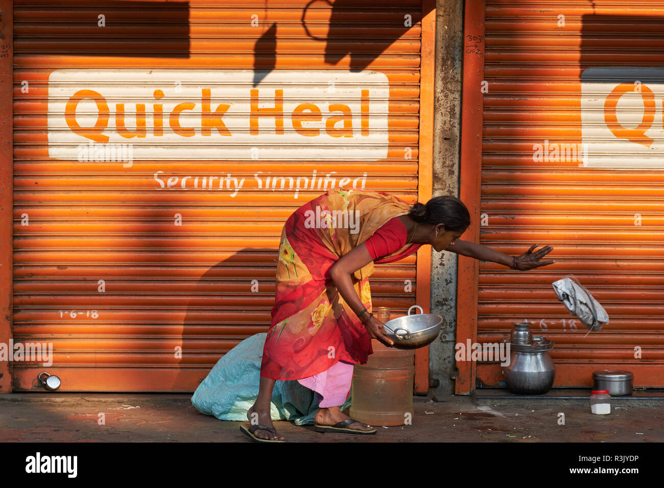 Eine so genannte Pavement dweller oder Obdachlosen in Kalbadevi, Mumbai, Indien, das Vorbereiten der Nahrung und Clearing "Ihr" Bereich vor einem Geschäft Stockfoto