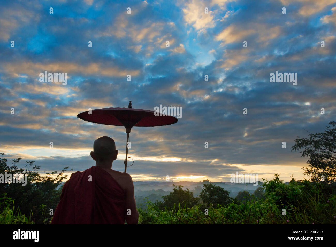 Mönch mit Regenschirm beobachten antiken Tempel und Pagoden im Dschungel bei Sonnenaufgang, Mrauk-U, Rakhine State in Myanmar Stockfoto