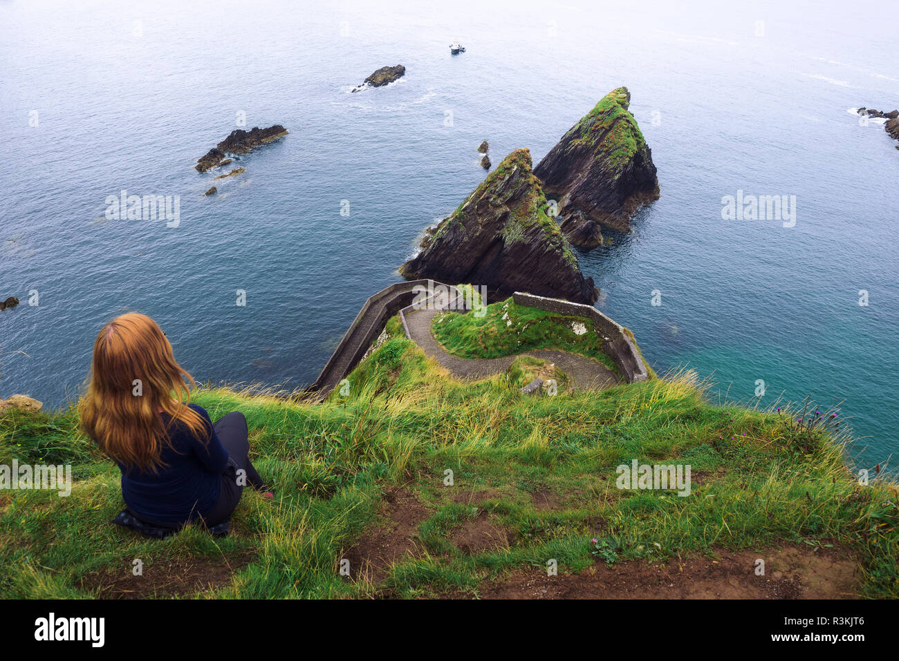 Mädchen sitzt auf einem Felsen über dem Ozean in Irland Stockfoto