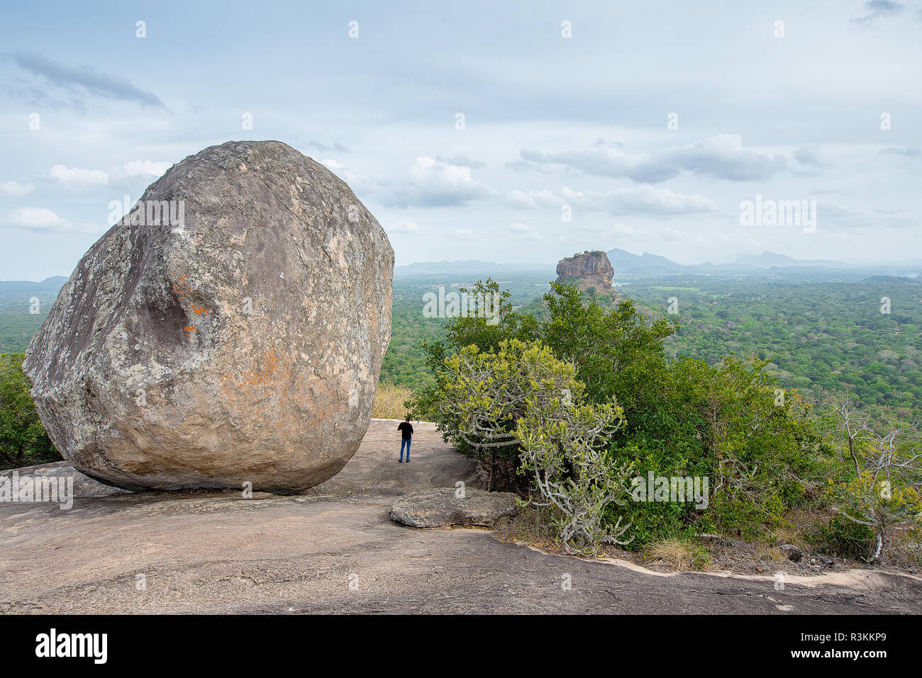 Eine Person, die die Ansichten der Lion Rock in Sigiriya hinter einem Felsen von Pidurangala, Sri Lanka Stockfoto