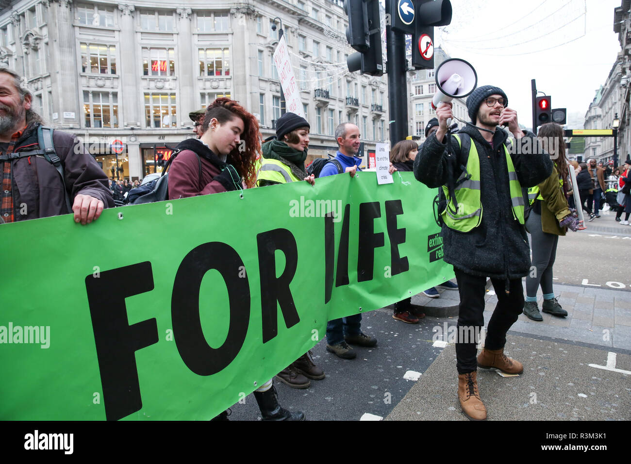 London, UK, UK. 23 Nov, 2018. Einen Mann beobachtet, als er auf einem Megaphon während des Protestes. Aussterben Rebellion Demonstranten Oxford Street Junction halten den Verkehr auf Black Friday Sales Tag blockieren. Credit: Dinendra Haria/SOPA Images/ZUMA Draht/Alamy leben Nachrichten Stockfoto