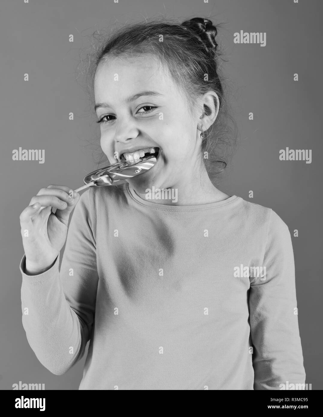 Mädchen isst großen bunten süßen Karamell. Dame hält, runde Lutscher. Kind mit glücklichen Gesicht wirft mit Süßigkeiten auf grünem Hintergrund. Glück und dess Stockfoto