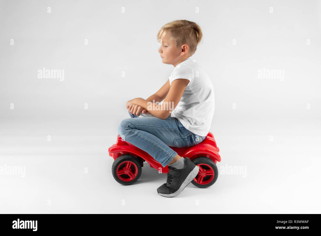 Kleine blonde Junge sitzt auf einem Spielzeug Fahrzeug ein Denken ist Stockfoto