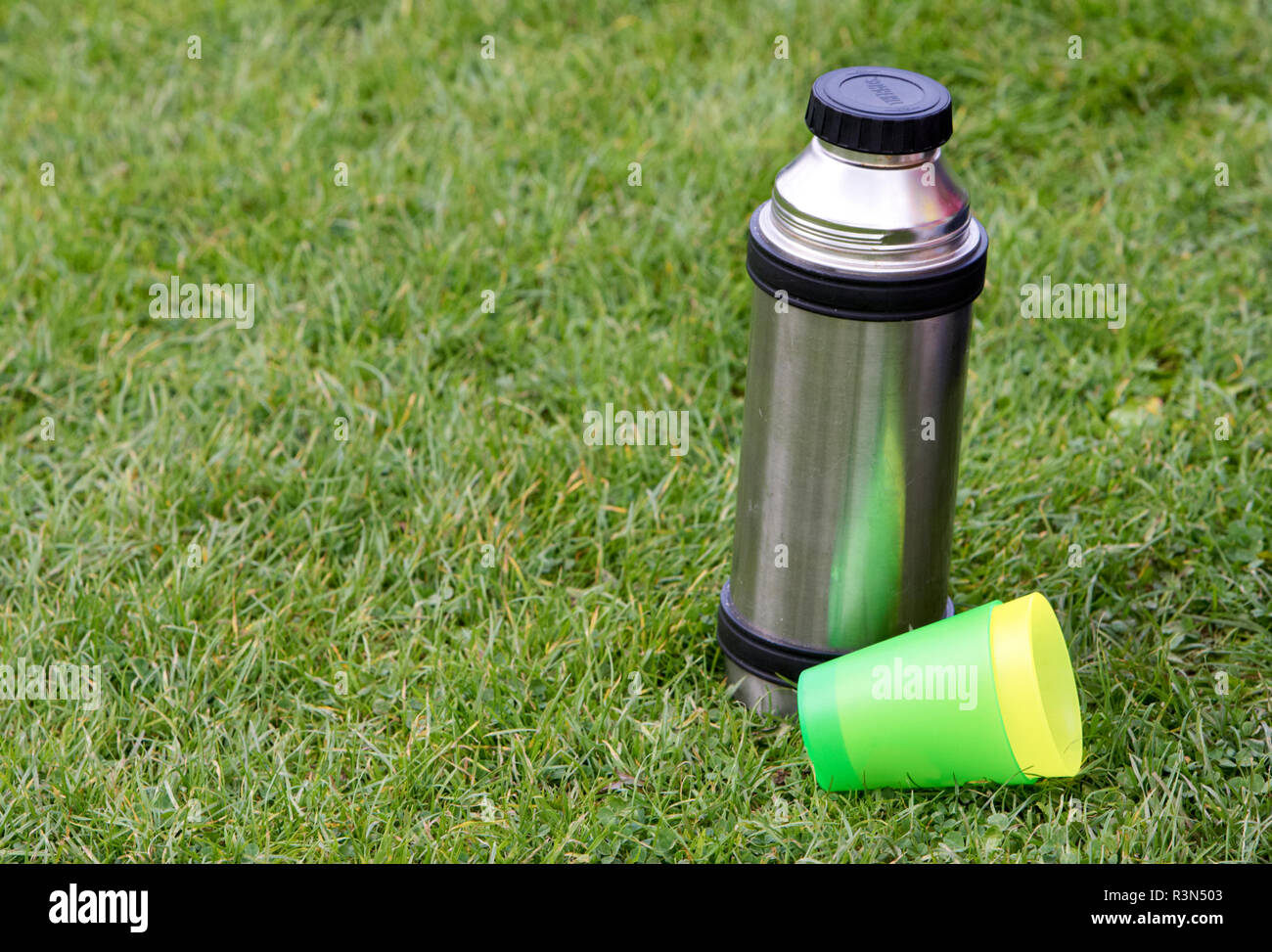 Metall Thermoskanne auf Gras mit zwei Plastikbechern außerhalb im Sommer Getränke kühl halten. Stockfoto