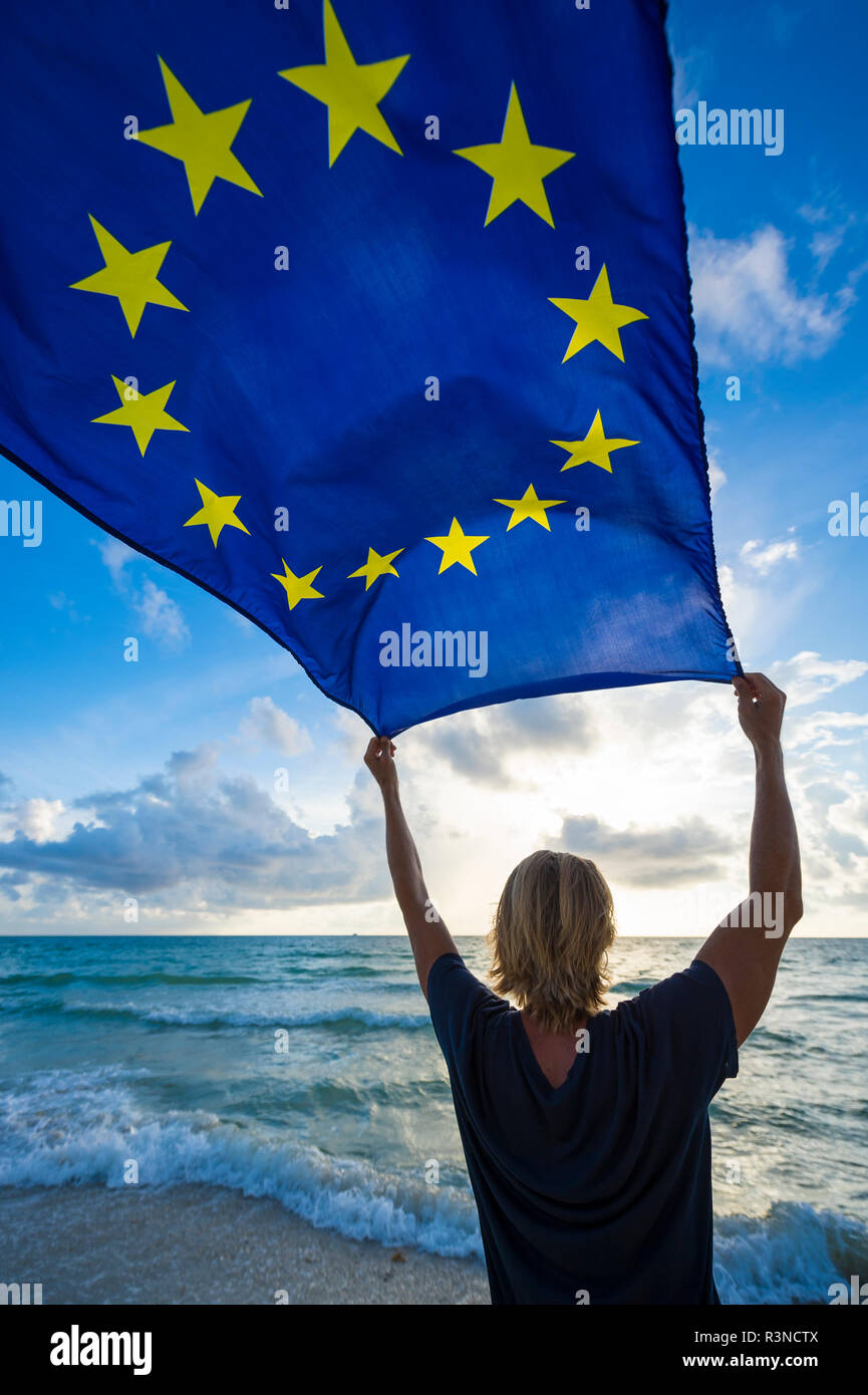 Fahne der Europäischen Union in den hellen Morgen Sonnenlicht durch Mann mit blonden Haaren auf leeren Strand am Mittelmeer statt Fliegen Stockfoto