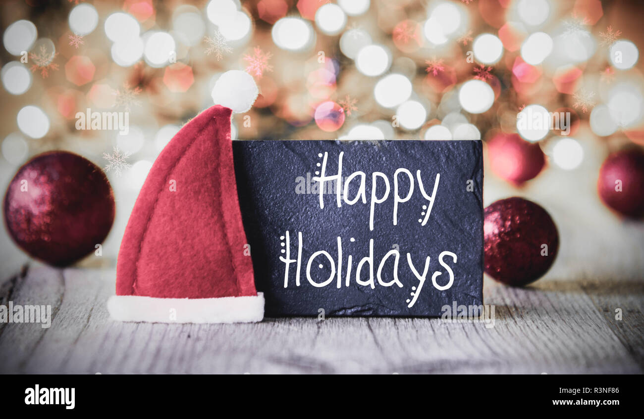 Mit englischen Kalligraphie frohe Feiertage. Funkelnden und glitzernden Lichter Hintergrund. Weihnachtsdekoration wie Lila Kugeln und Santa Hat Stockfoto