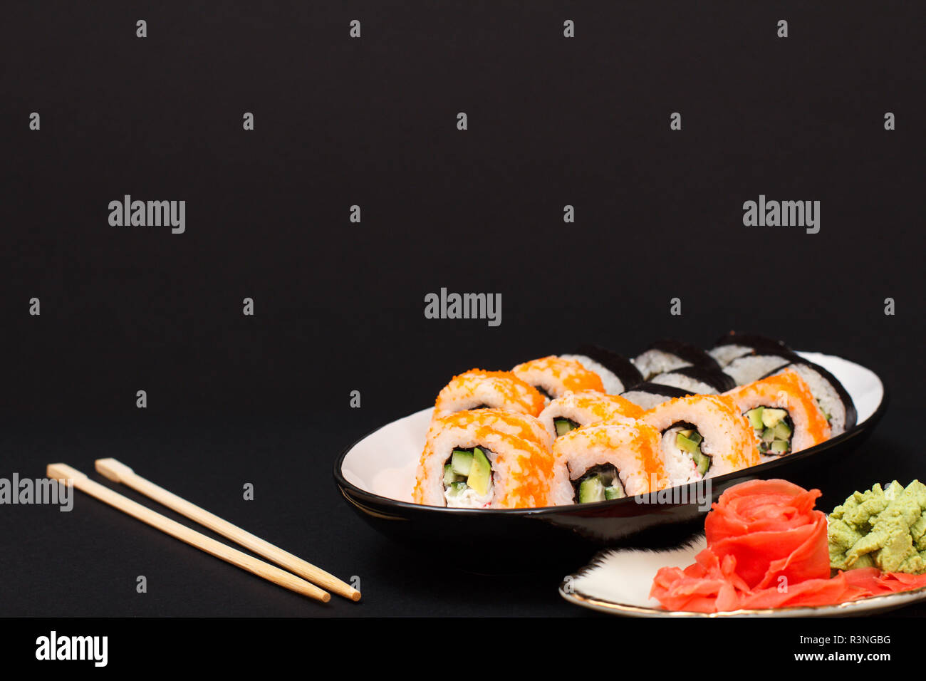 Sushi Rollen mit Nori, Reis, Avocado, Gurke, fliegende Fische roe auf Keramikplatte. Mit roten eingelegten Ingwer und Wasabi. Schwarzer Hintergrund Stockfoto