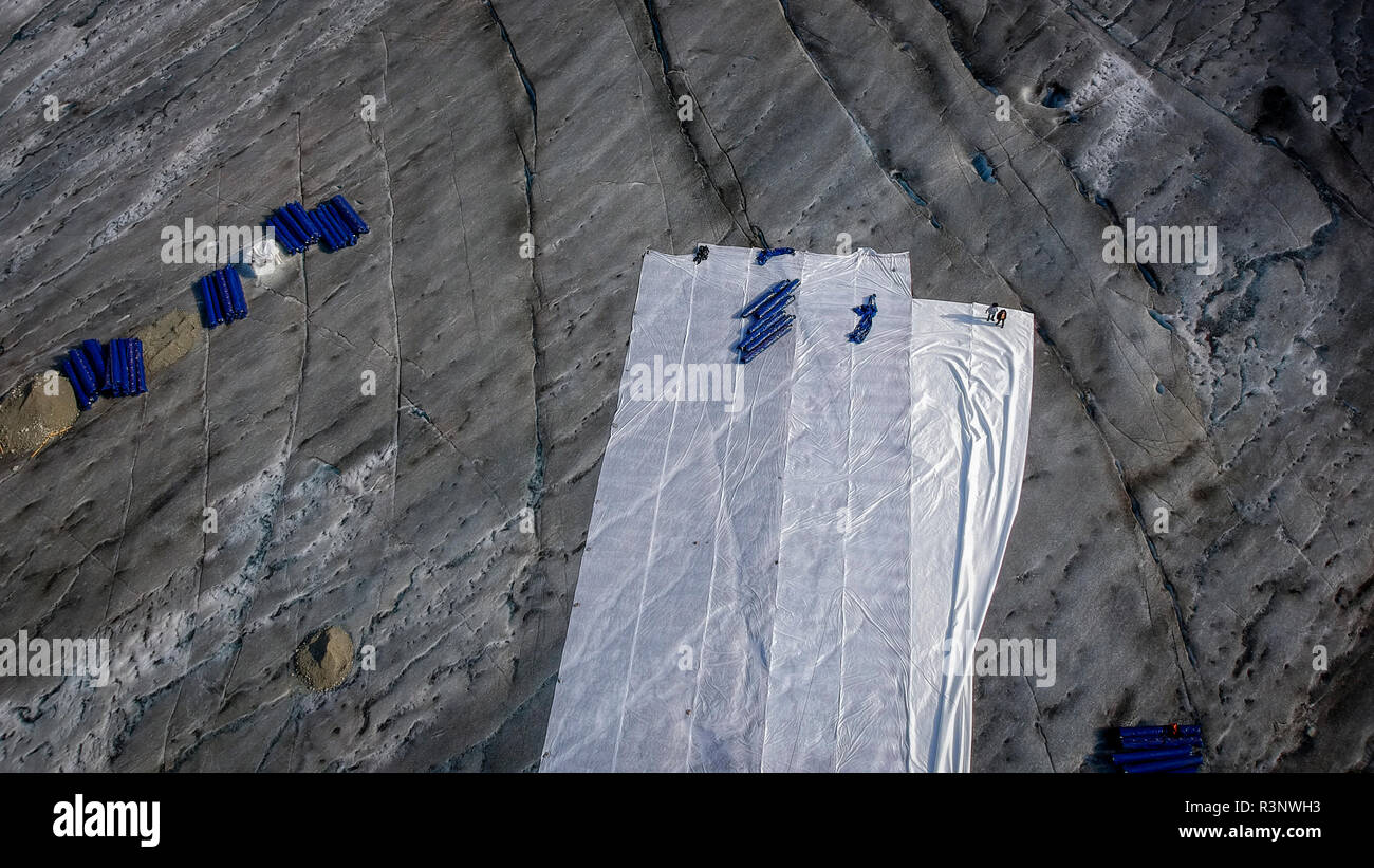 Klima Rhone: Riesige Fleecedecken bedecken Teile des Rhonegletschers in der Schweiz, um das unvermeidliche Schmelzen von Schnee und Eis zu vereizen. Nach einem Winter mit Rekordschneemengen war der größte Teil davon verschwunden, als dieses Bild am 14. Juli 2018 aufgenommen wurde, das das dunklere Eis freilegt. Während Schnee ein brillanter Reflektor der Sonnenenergie ist, absorbiert das dunklere Eis stattdessen die Energie und beschleunigt so das Schmelzen des Gletschers. Die Farbe und Dunkelheit des Gletschereises variiert weltweit, je nach Verschmutzungsbildung, Alter des Eises, vom Eis und vom Mikro aufgepflückten Partikeln Stockfoto