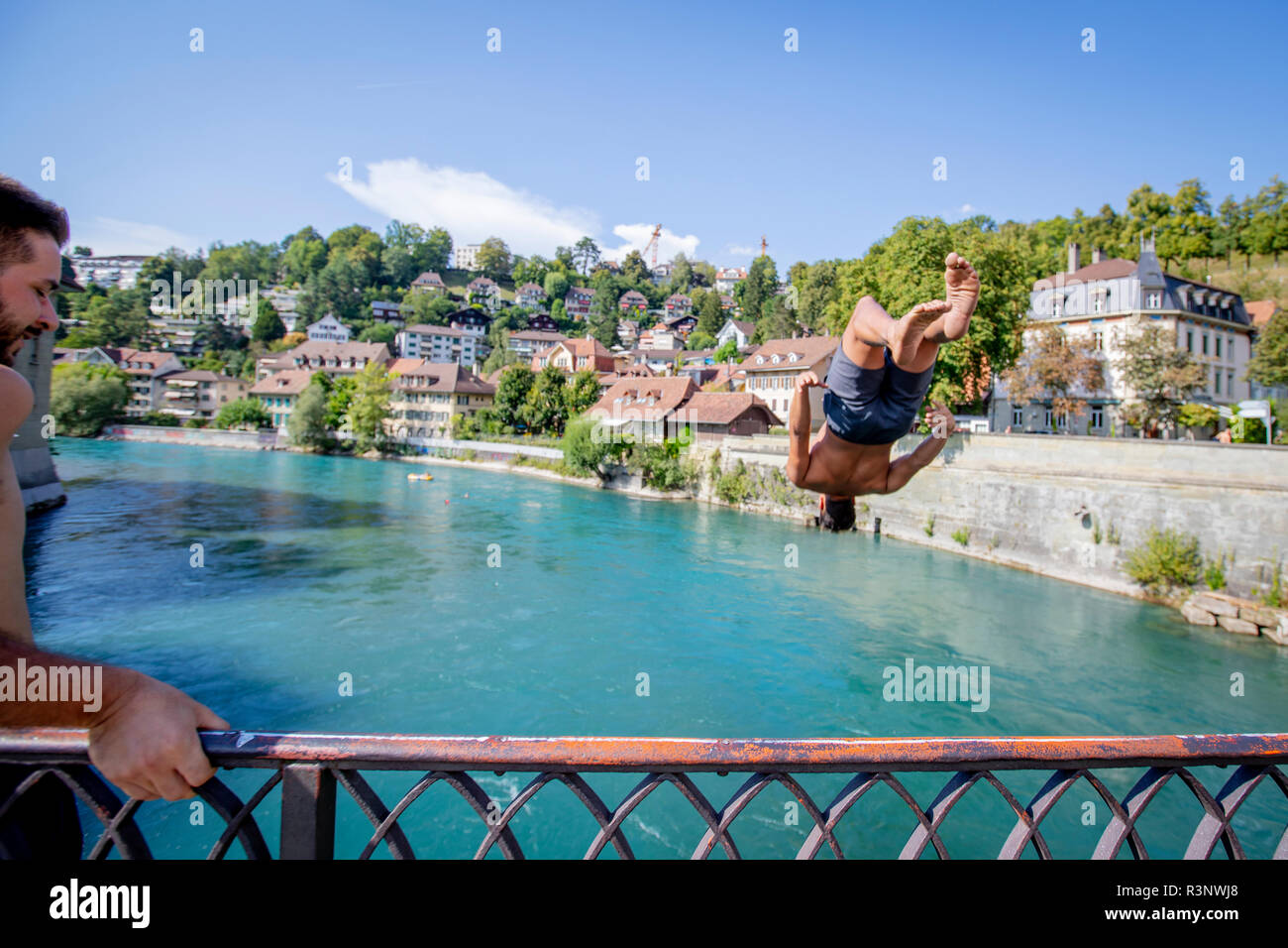 Ein Mann springt in einem Rückwärtssalto vom Untertor Brucke in Bern. Die Aare schwebt direkt durch die Schweizer Hauptstadt Bern, und sobald die Temperatur über 10 Grad kriecht, sieht man, wie die Menschen zum Schwimmen ins Wasser springen. Viele nutzen den Fluss regelmäßig, um zum Mittagessen oder zur Arbeit zu schwimmen. Einige schwimmen sogar das ganze Jahr über. Stockfoto