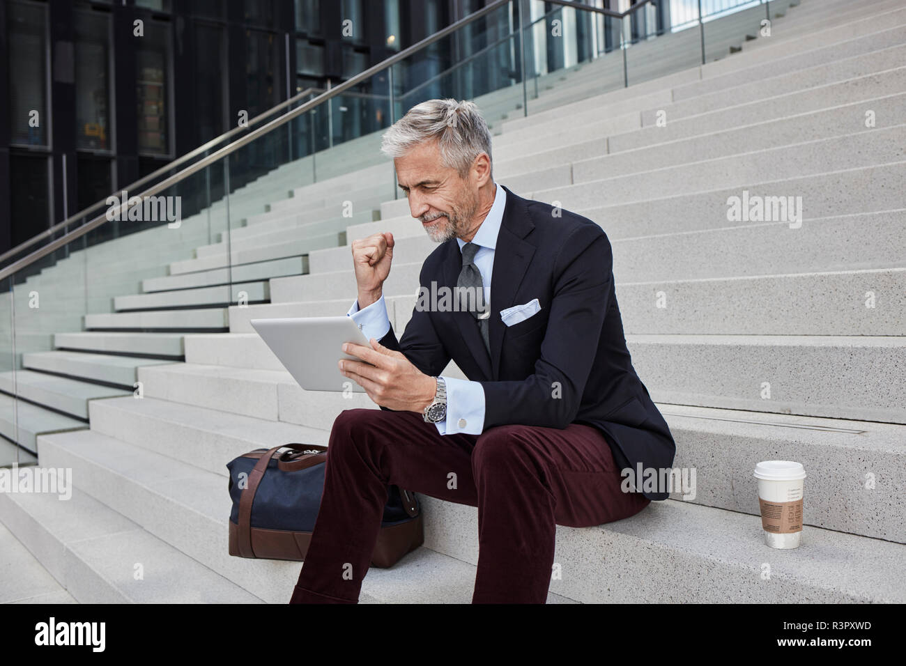 Modische Geschäftsmann mit Reisetasche nd Kaffee sitzen auf der Treppe mit Tablette zu gehen Stockfoto