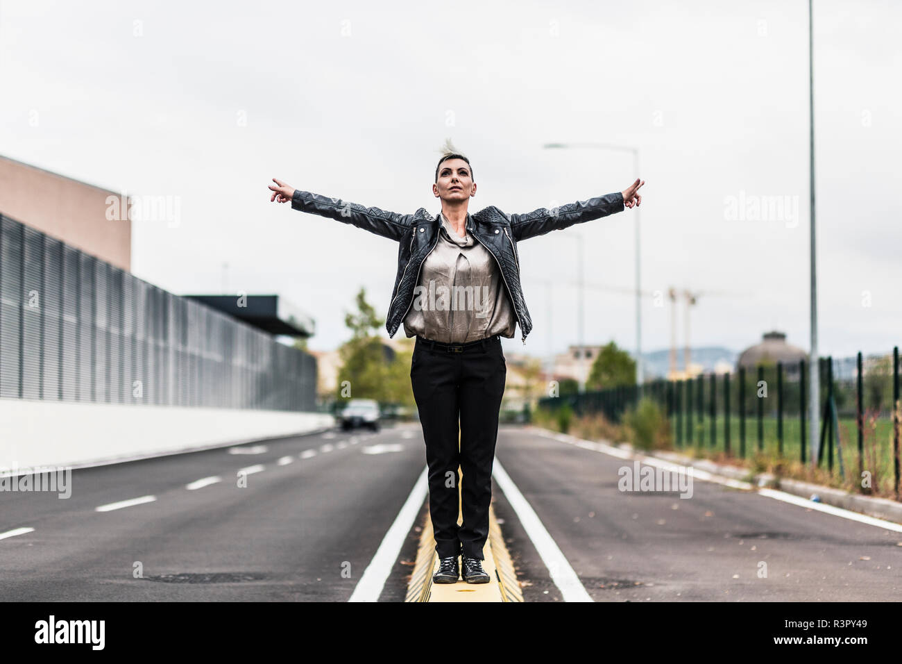 Punk stehende Frau auf eine Barriere am Straßenrand mit ausgestreckten Armen Stockfoto
