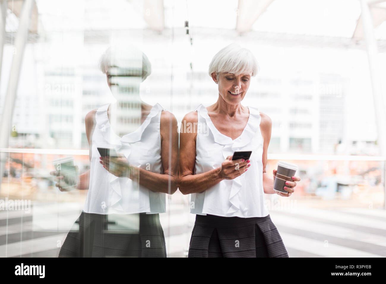 Lächelnde ältere Frau mit Handy und Kaffee zum Mitnehmen im Freien Stockfoto