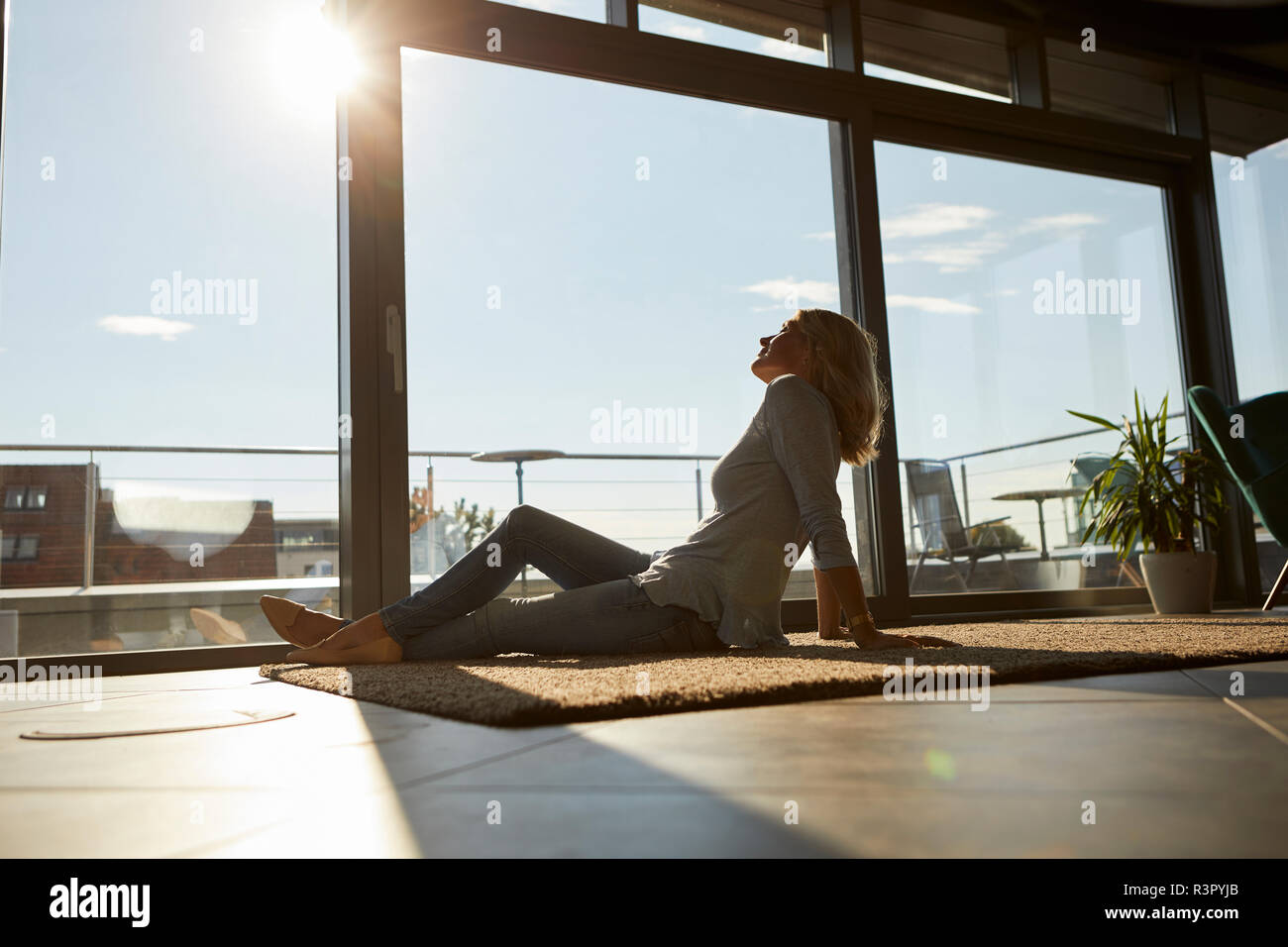 Entspannt reife Frau sitzt auf dem Teppich im Sonnenlicht zu Hause Stockfoto