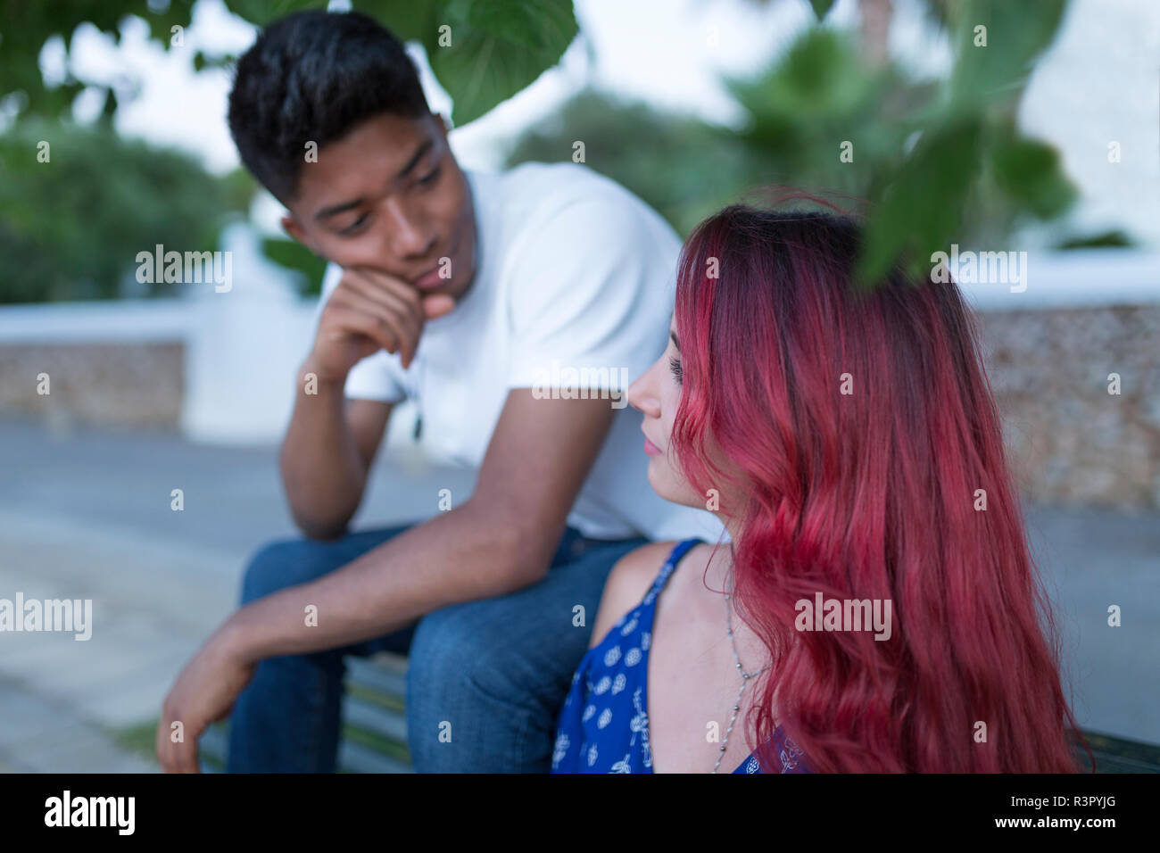 Junge Frau mit rot gefärbten Haaren sitzt auf der Bank mit ihrem Freund Stockfoto