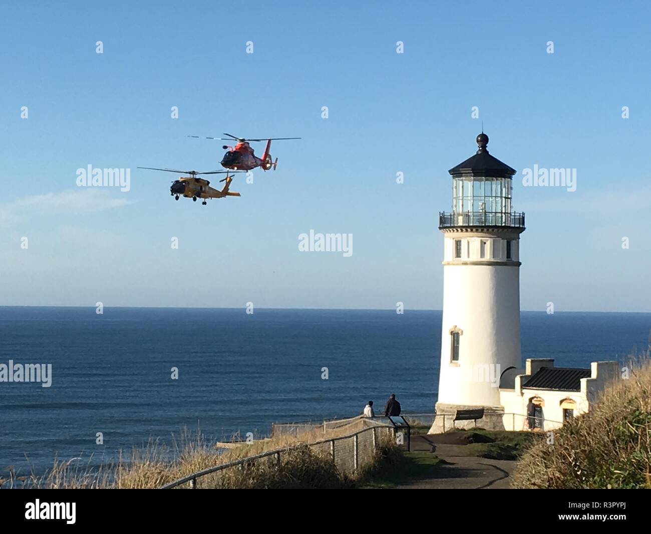 Besatzungen an Bord MH-65 Dolphin und MH-60 Jayhawk Helikopter fliegen vorbei am North Head Lighthouse in Fez, Washington, nach Abschluss cliff Rescue Training in Kap Enttäuschung State Park in Fez, Washington Nov. 7, 2018. Die Klippe rescue Training war auf den Klippen unter der Leuchtturm mit Blick auf Benson Strand durchgeführt. U.S. Coast Guard Foto von Senior Chief Petty Officer Eric Bednorz. Stockfoto